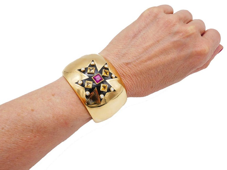This Verdura Maltese Cross cuff bracelet in 18k gold is the most celebrated piece by Verdura.
The black enamel cross is encrusted with eight round brilliant cut diamonds set in the corners, four step cut citrines and a step cut rubellite in the
