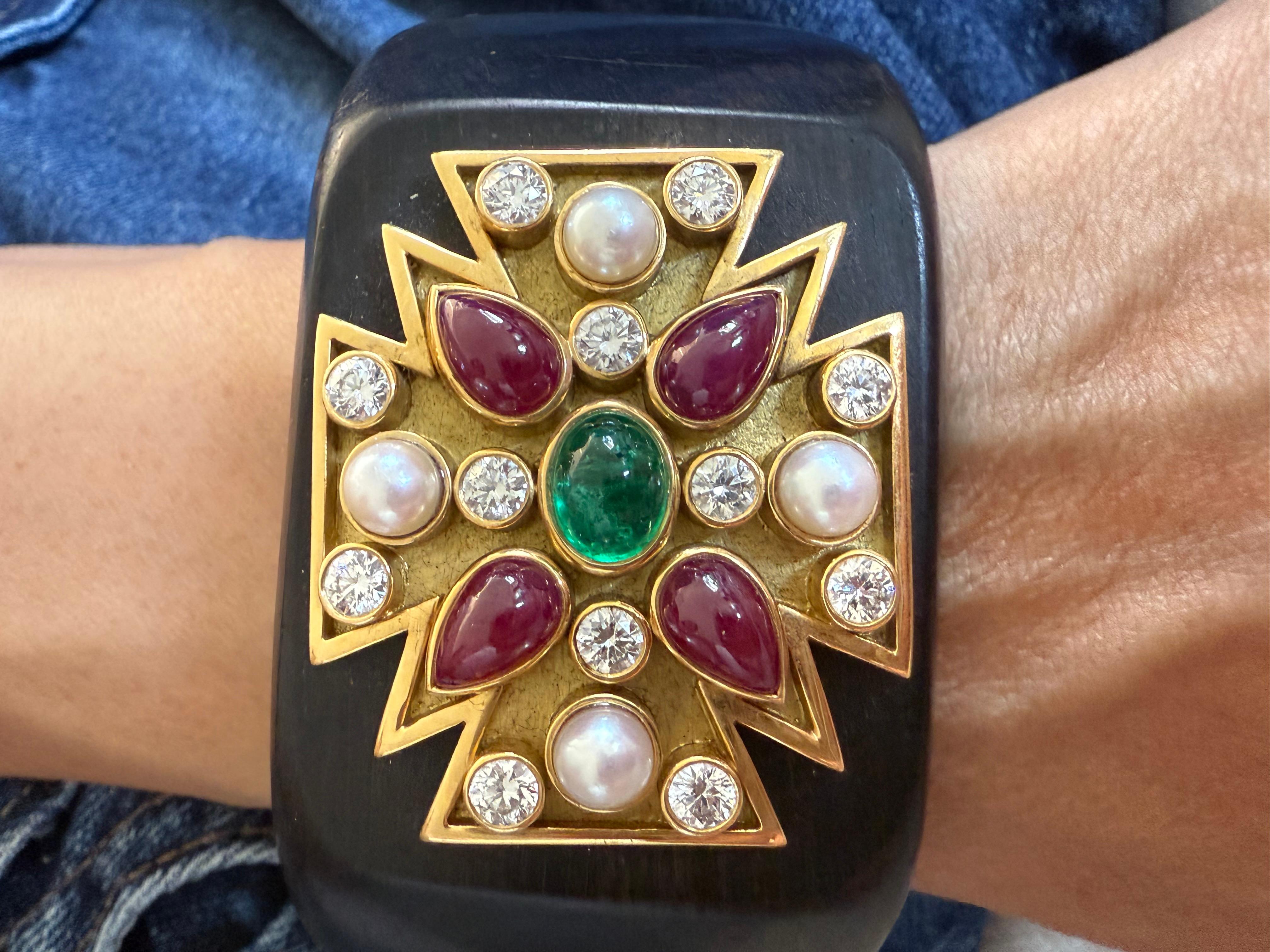 The Verdure Maltese Cross Cuff with Diamonds Cabochon Rubys and emerald center with 12 round diamonds  set an 18 k yellow gold a top a wood cuff bracelet. 
1.75 inches in width and will fit a medium + size wrist.
Approximately 3cts of white diamond