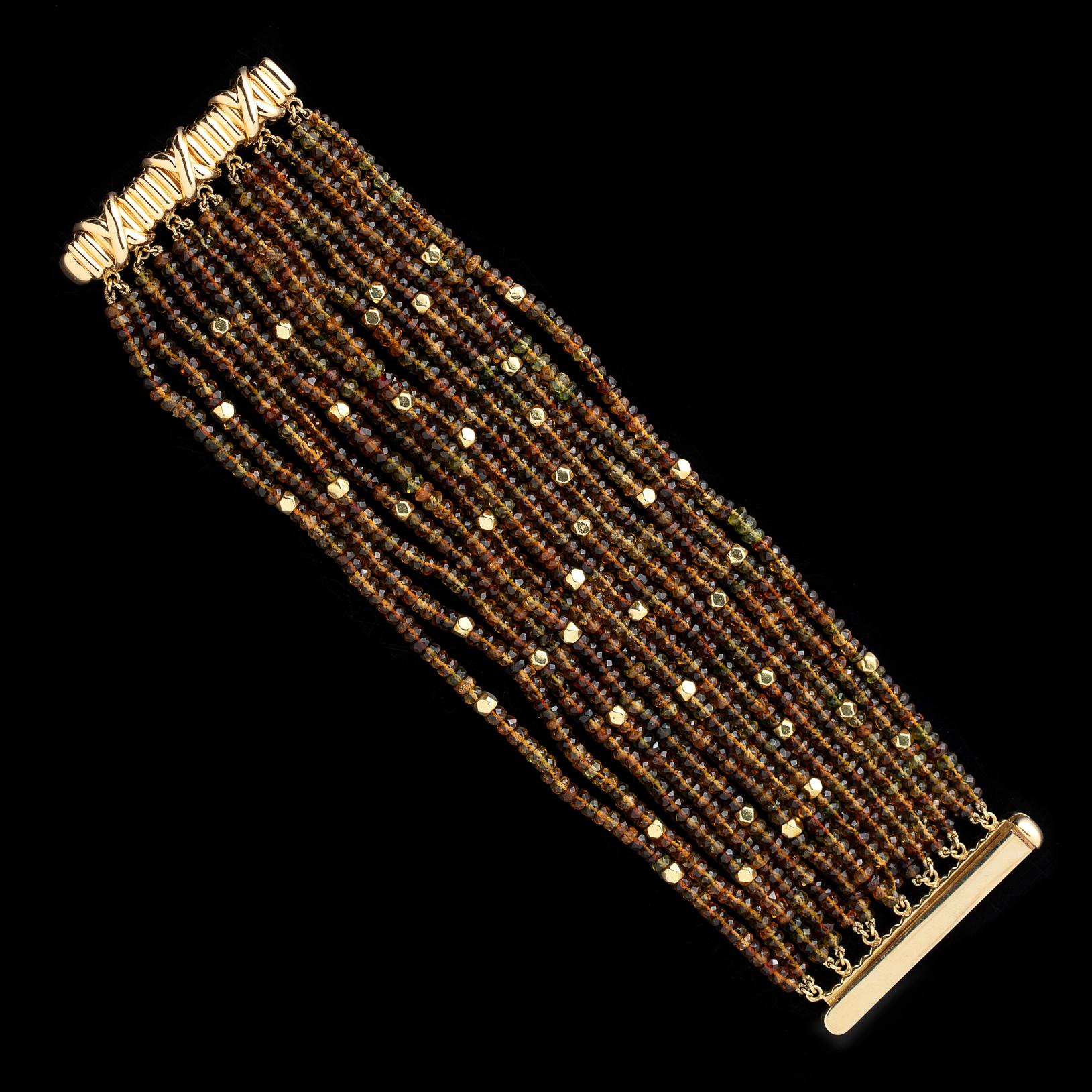 Circa 2000, the wide Verdura 18k yellow gold bracelet is designed with 14 rows of faceted roundel citrine and peridot beads, and further accented with gold faceted beads. The bracelet measures 7 1/4 inch in length, is 2 inches wide, and is