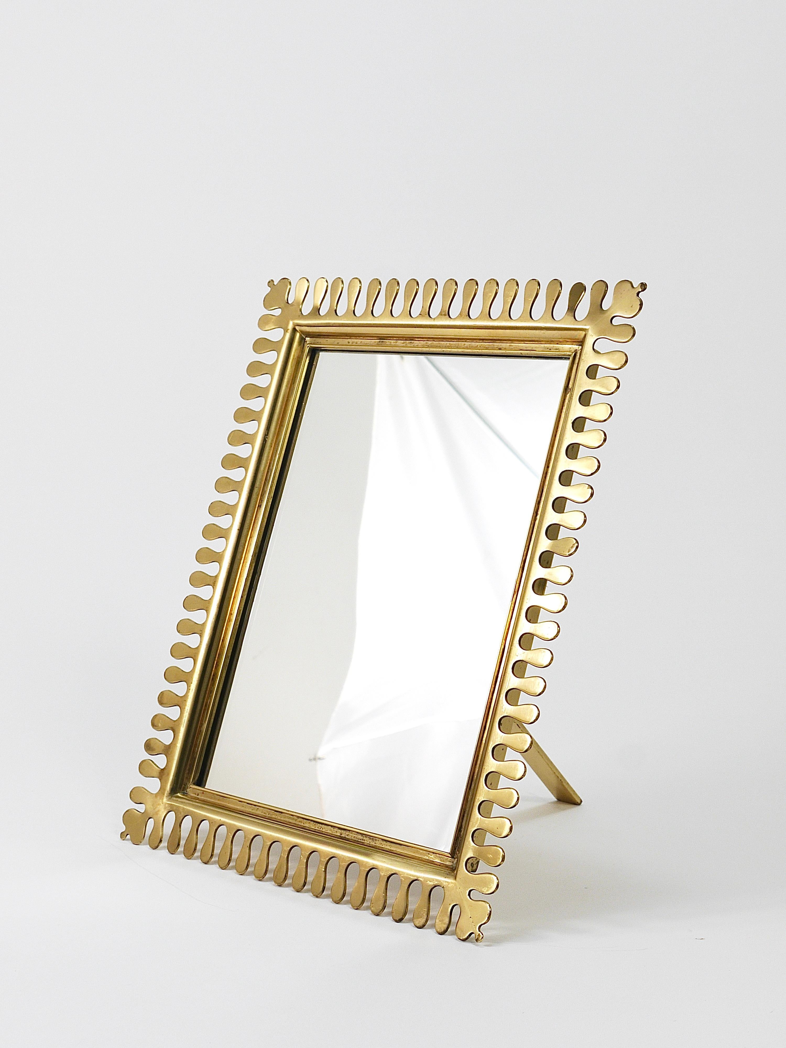 A fine and elegant brass mirror from the 1970s, crafted by Vereinigte Werkstätten München in Munich, Germany. This lovely Mid-Century mirror can be used as a tabletop vanity mirror or as a wall mirror. The scalloped edging on the solid brass frame