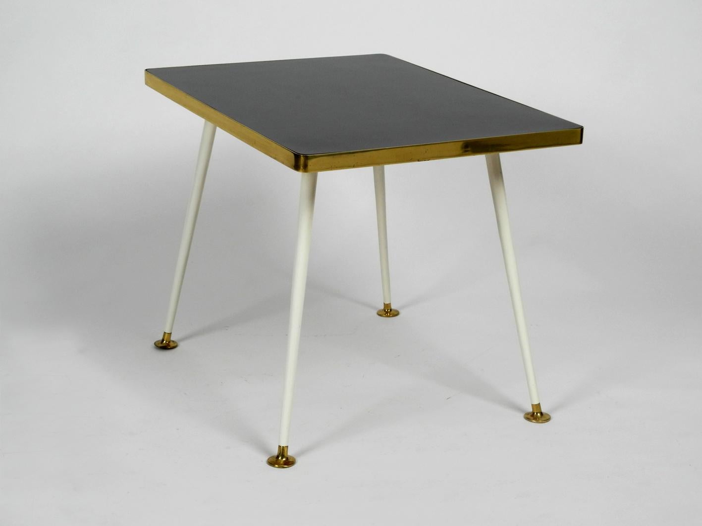 Very rare and pretty Mid Century Modernist side table. Great minimalistic rare design from the Vereinigte Werkstätten.
Solid wood top with resopal surface. Edges are made of solid brass. Metal legs are white lacquered. Feet are made of brass.
Very