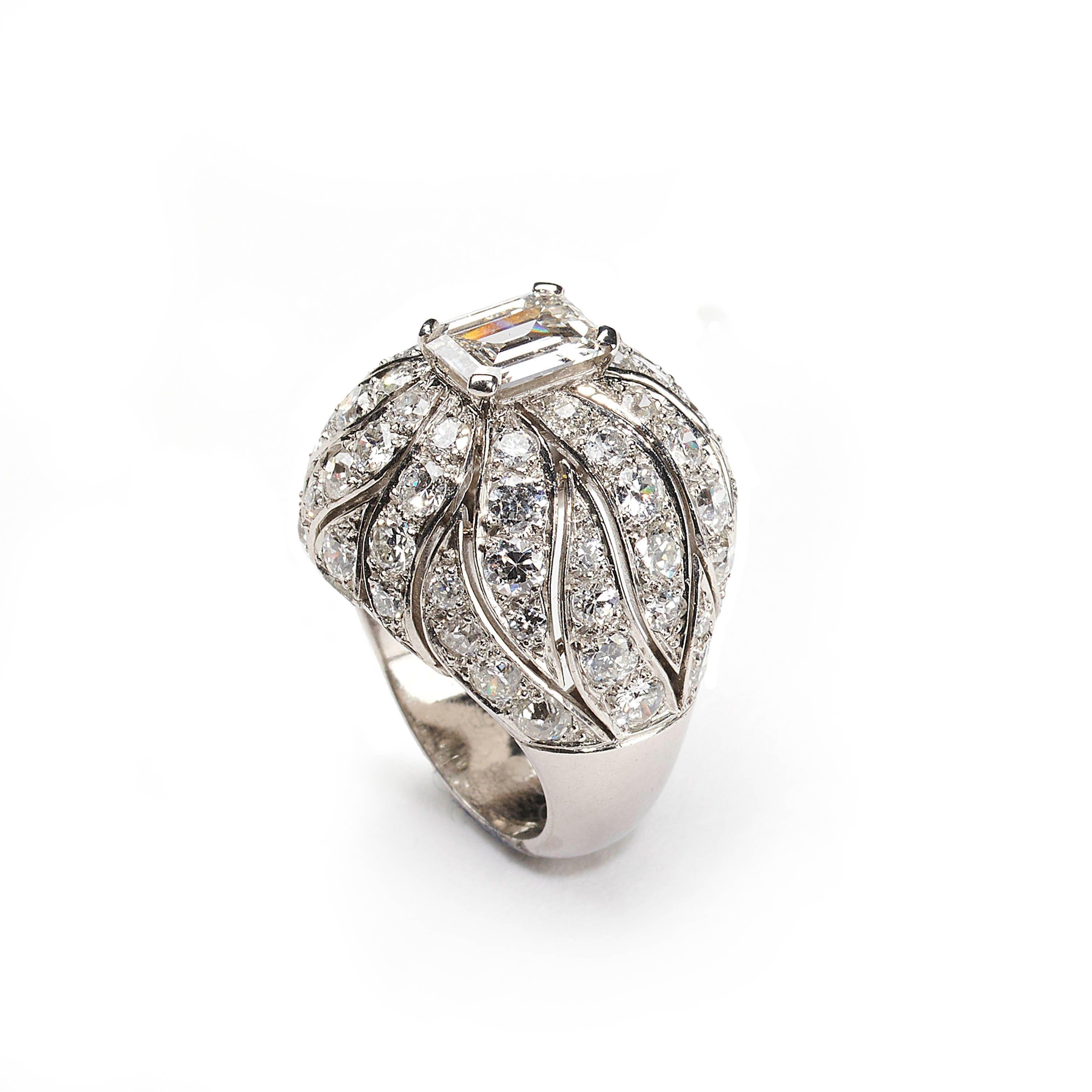 A Verger & Cie vintage bombé diamond ring, with a 1.24ct, J colour, SI2 clarity emerald-cut diamond, in a four claw setting, in the centre of an openwork, round brilliant-cut diamond set, flame like design, on bombé shoulders, on a solid, D shaped,