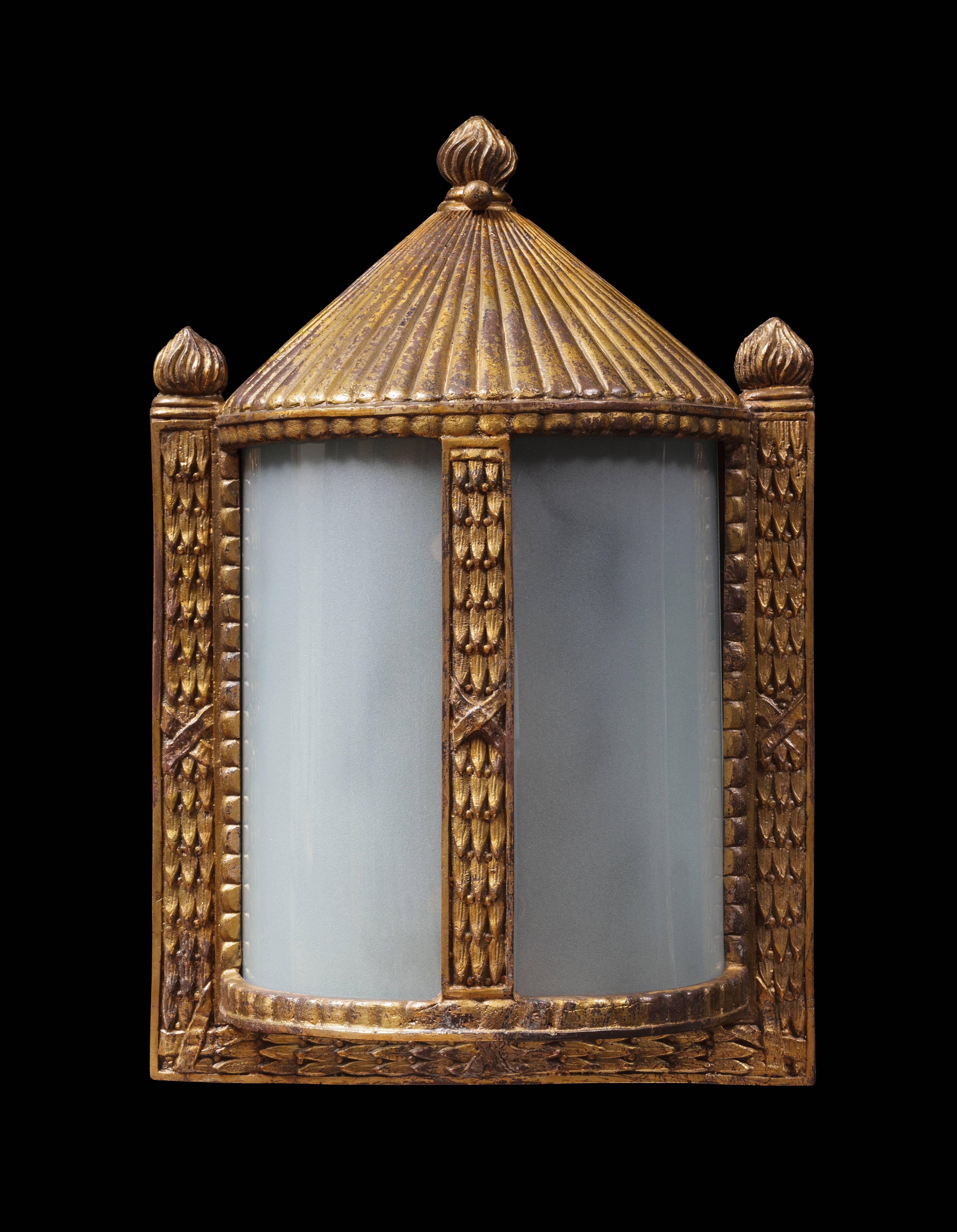 Drawing on the decorative style of late the 19th century, this wall lantern of semi cylindrical form is framed with moulded bronze fasces, a tent-like top and three stylised flames.