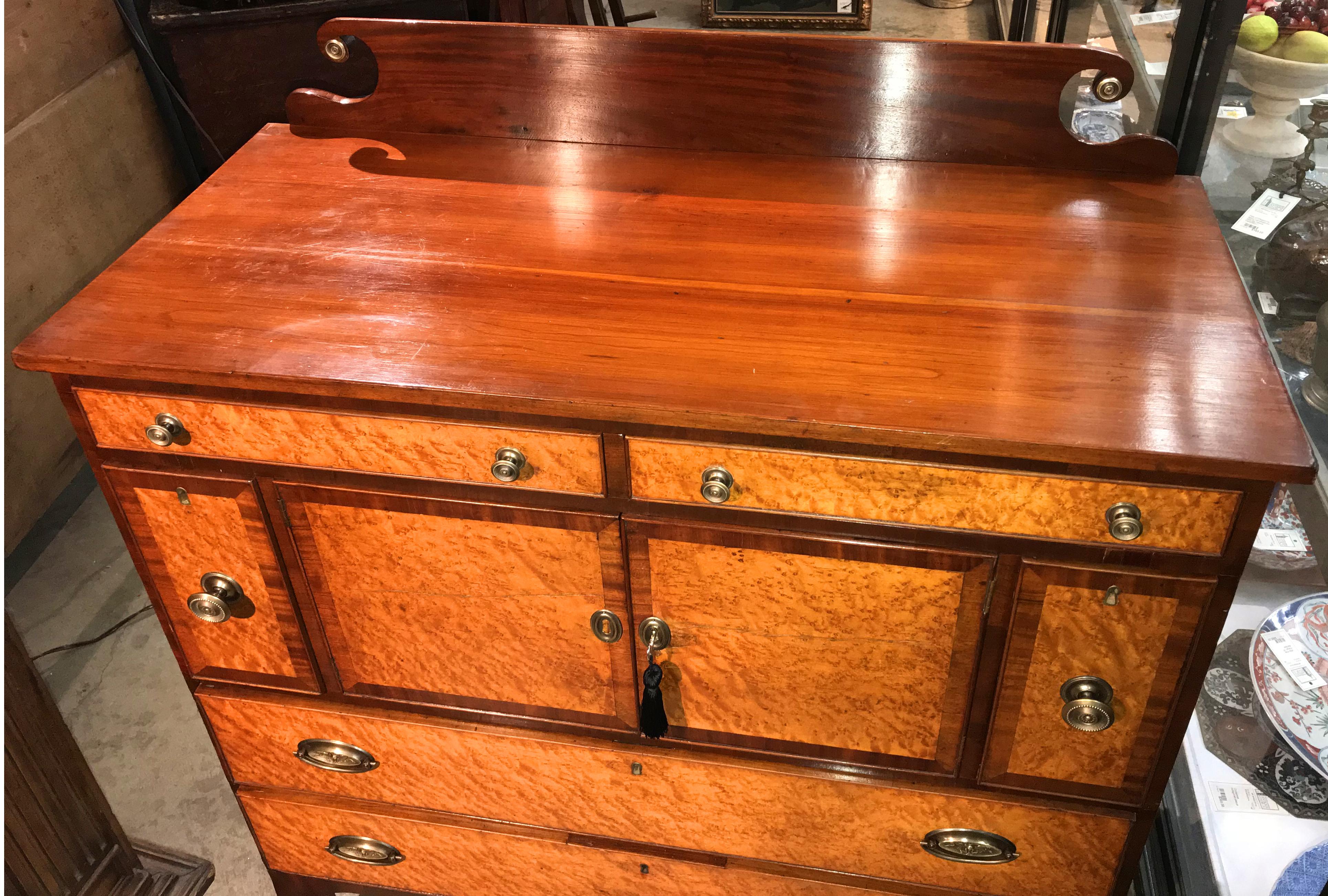 A fine example of a Federal cherry server or sideboard with rectangular top, shaped backsplash with brass bulls eyes, surmounting two fitted frieze drawers over a two-door central storage compartment, flanked by two bottle drawers, over two long
