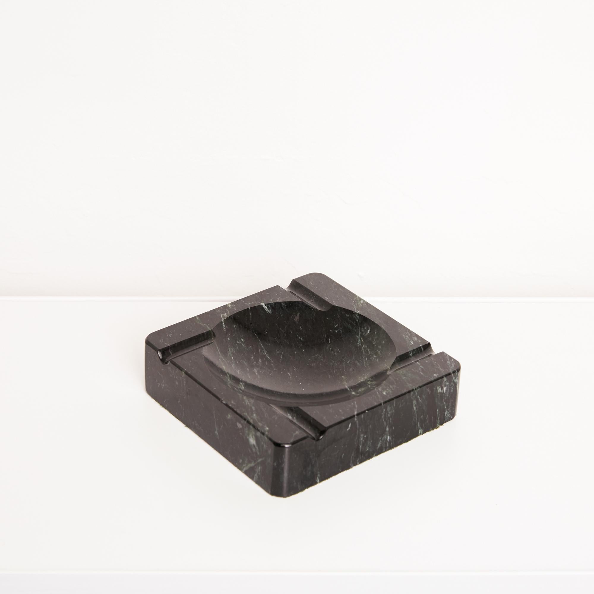 A square ashtray in a polished black marble with green and white veining by the Vermont Marble Company of Proctor, VT. The piece has a circular well, and four routed asymmetrical indentations perpendicular to its edges. The corners and edges of the