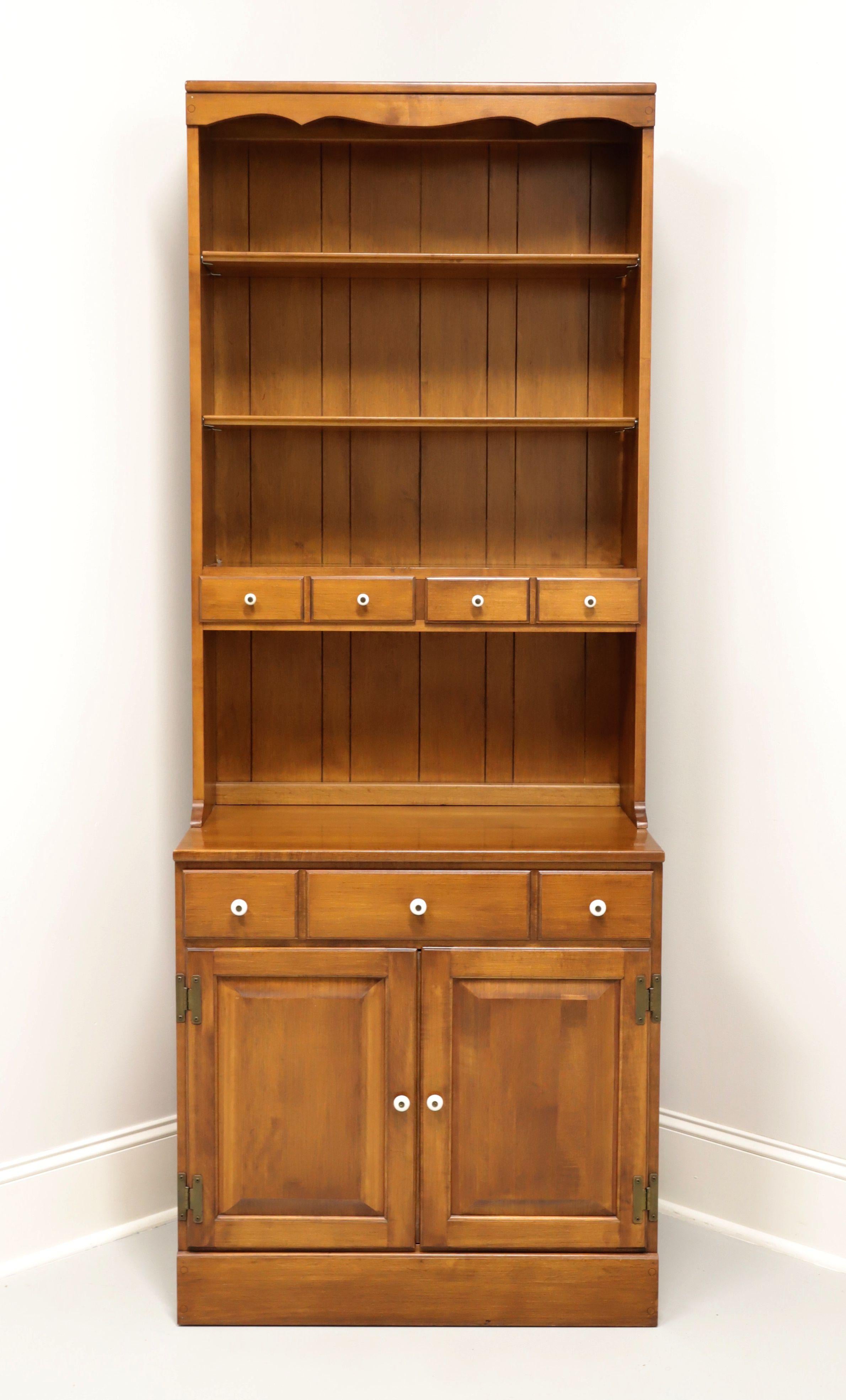 A Colonial style bookcase with cabinet by Vermont of Winooski. Solid rock maple with enamel knobs and brass hardware. Features upper stepback bookcase with plank back, two adjustable plate grooved wood shelves and two small dovetail drawers. Lower