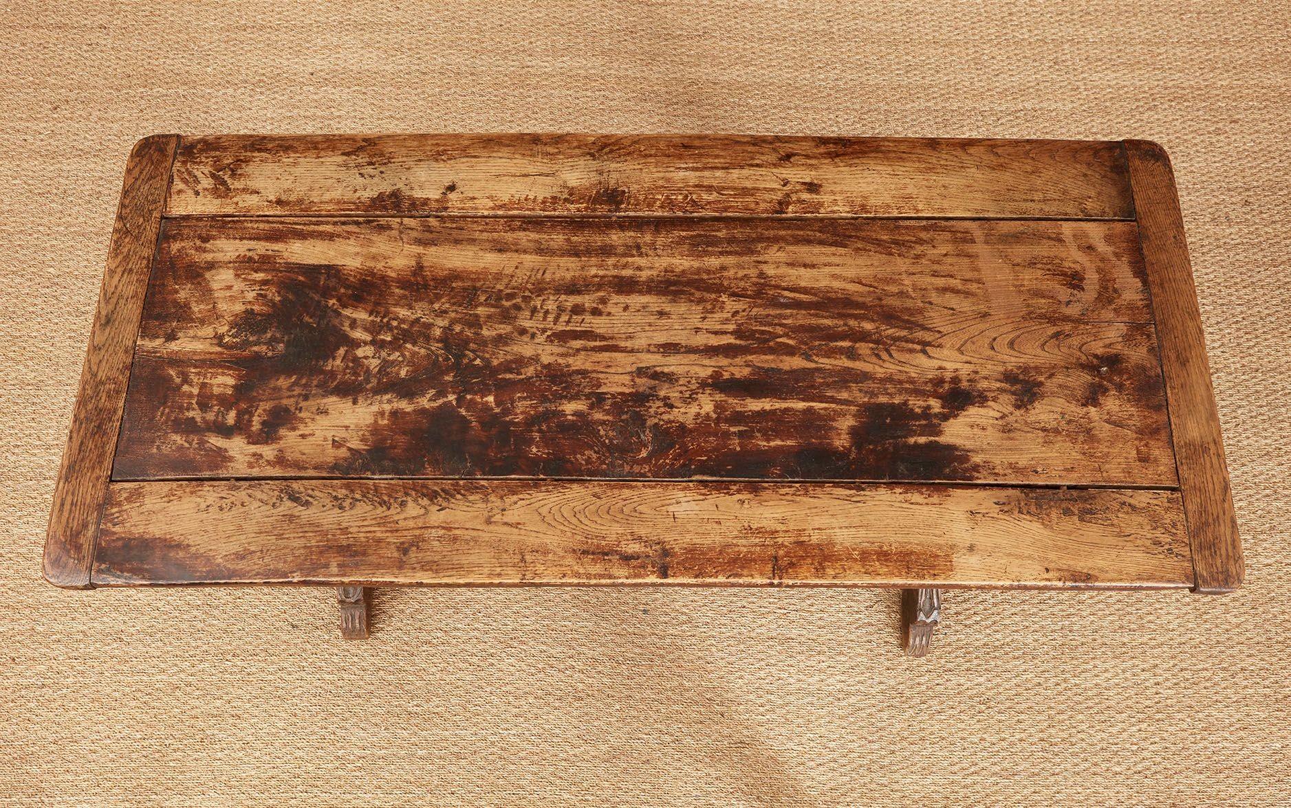 An English vernacular trestle table circa 1730 with extraordinary wide oak board top joined by breadboard edges over shaped and reinforced trestles with naively carved paw feet, the trestles joined by a stretcher retained by original turned wedges. 