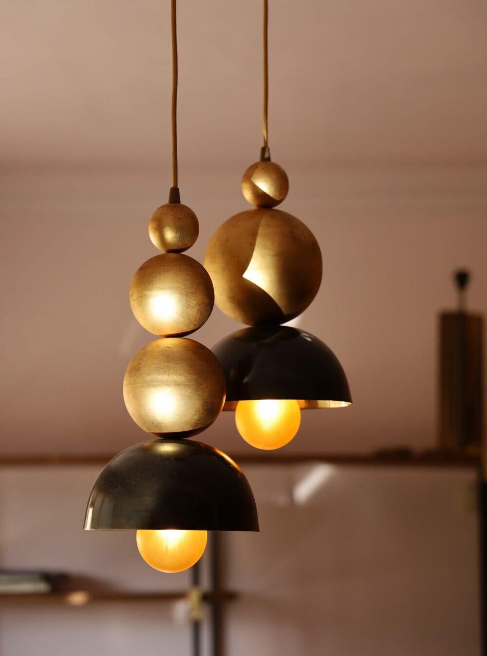 La lampada a sospensione Verner 2 presenta una composizione verticale di due elementi sospesi ad altezze sfalsate, riuniti sotto un'unica calotta. 

Ogni pendente è costituito da una pila di sfere rivestite in foglia d'oro, che si alternano tra