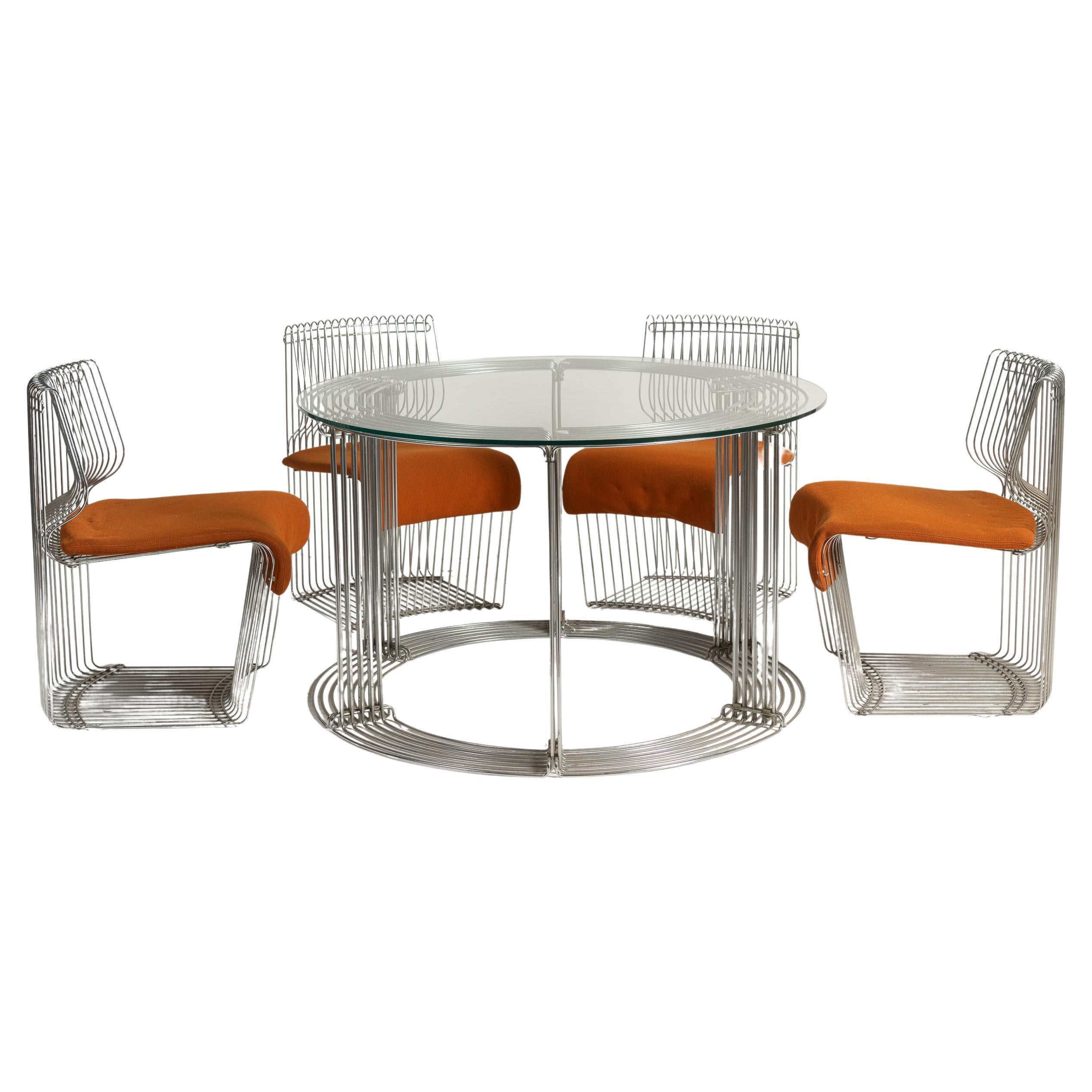 Le design innovant de Verner Panton associe un cadre élégant en fil d'acier à un plateau en verre pour créer une table vraiment moderne et élégante. Associé à quatre chaises d'appoint dotées d'une assise rembourrée amovible, cet ensemble incarne le
