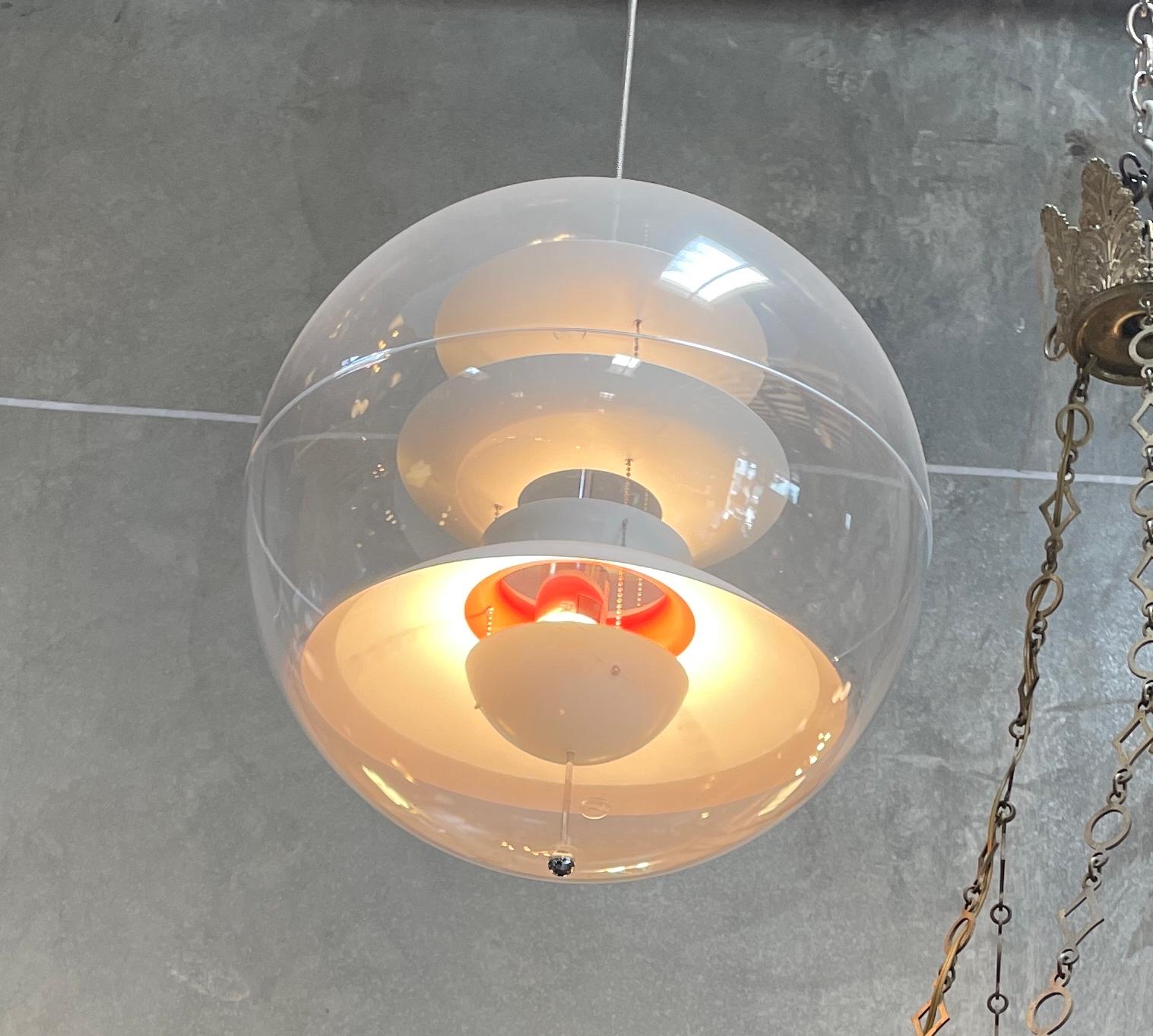 Production récente du design de Verner Panton datant de 1977, cette lampe suspendue se compose d'une sphère transparente en acrylique et de réflecteurs en aluminium blanc avec quelques parties intérieures rouges et émet une belle lumière diffuse. 