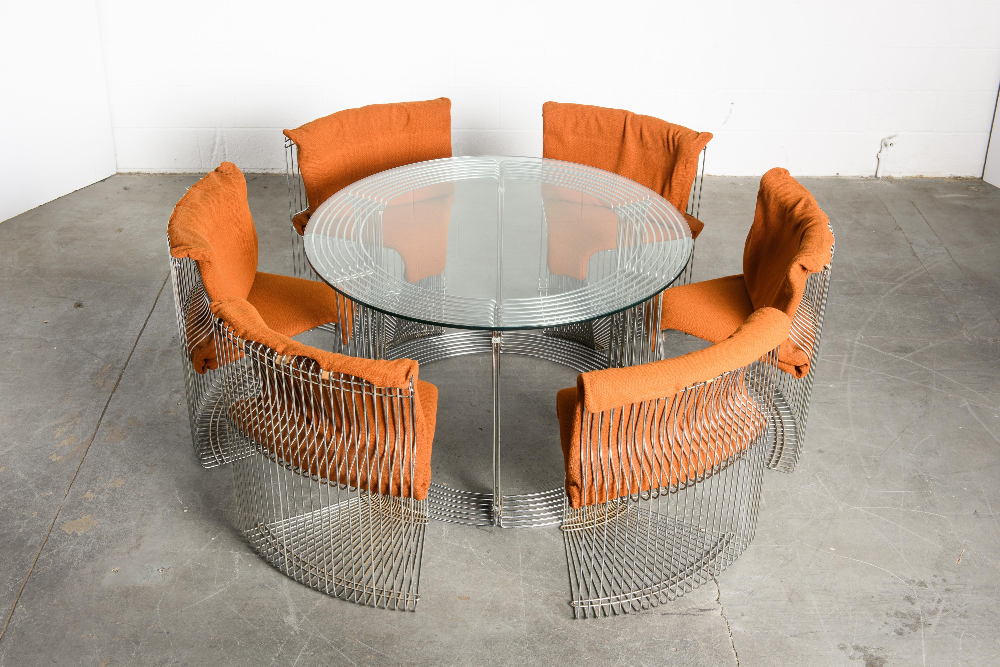 This original, early production year, 'Pantonova' dining room suite by Verner Panton for Fritz Hansen consists of six convex nickel-plated steel wire dining chairs which nest into its corresponding dining table with glass top. 

This Verner Panton