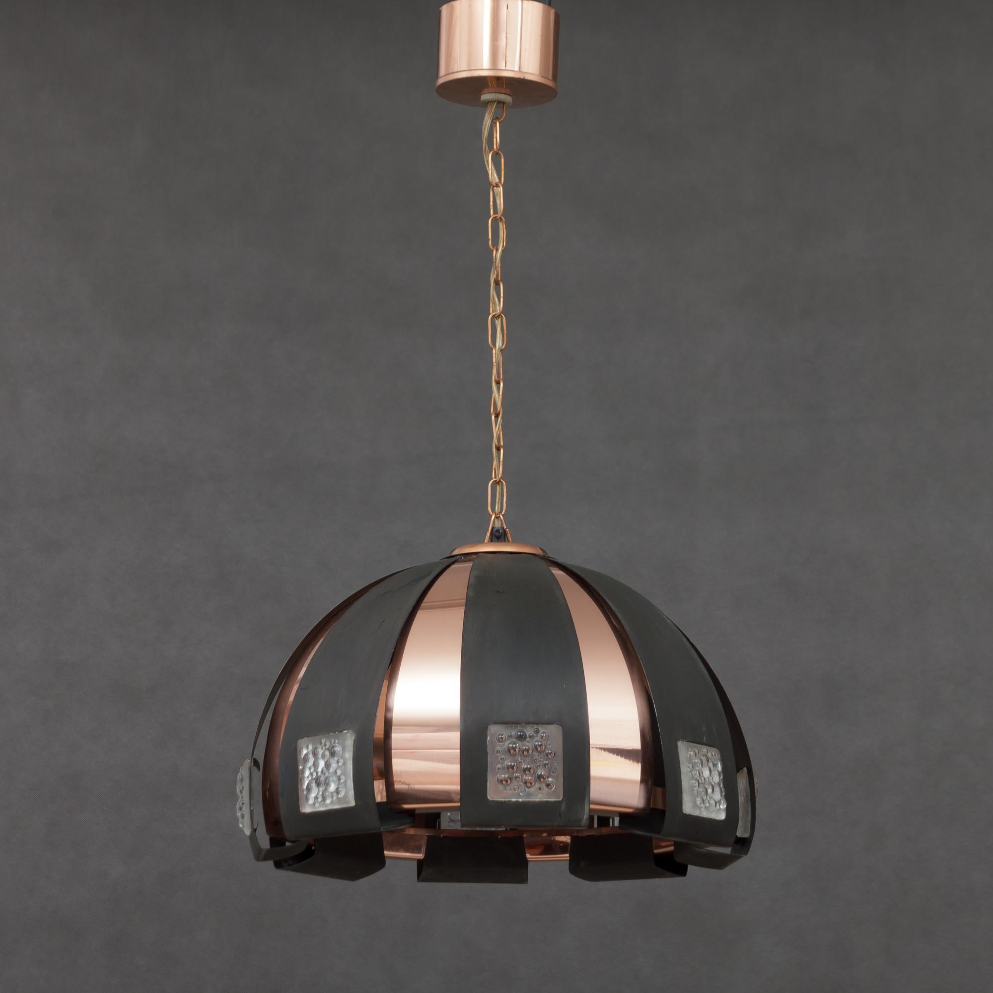 This pendant was designed by Verner Schou for Coronell Elektro in Denmark in late 1960s. It is made from interchanging black oxidized metal and copper stripes with mounted squares of opalescent bubble glass. As most of Shou’s light provides the