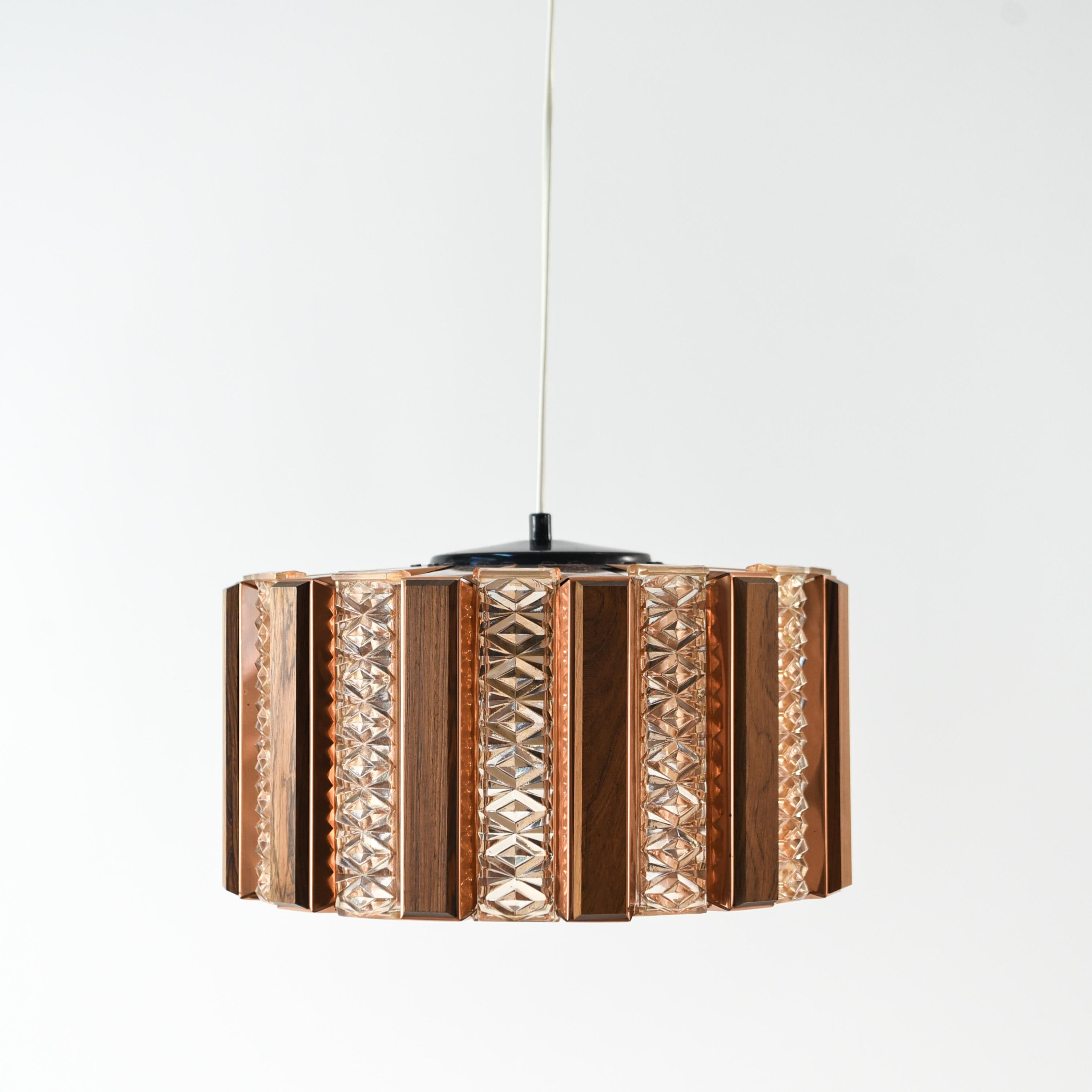 This rare chandelier was designed by Verner Schou for Coronell Elektro and features panels of Orrefors glass amidst the typical copper which adds to its unusual quality.
