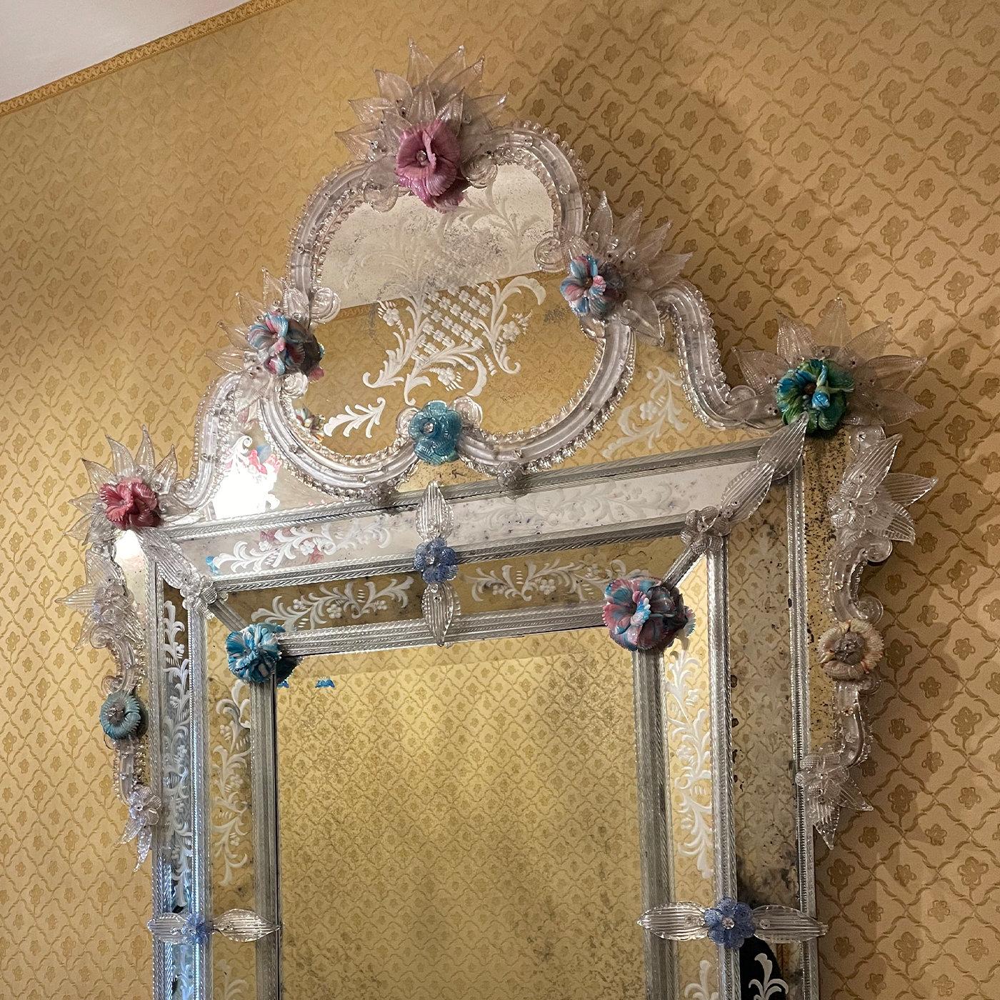 An array of leaves and frond details in antique-finished crystal embellish the sinuous frame of this sublime, one-off mirror handcrafted by Venetian master glassmakers. The three-dimensional flower inserts in multicolored glass paste add a touch of