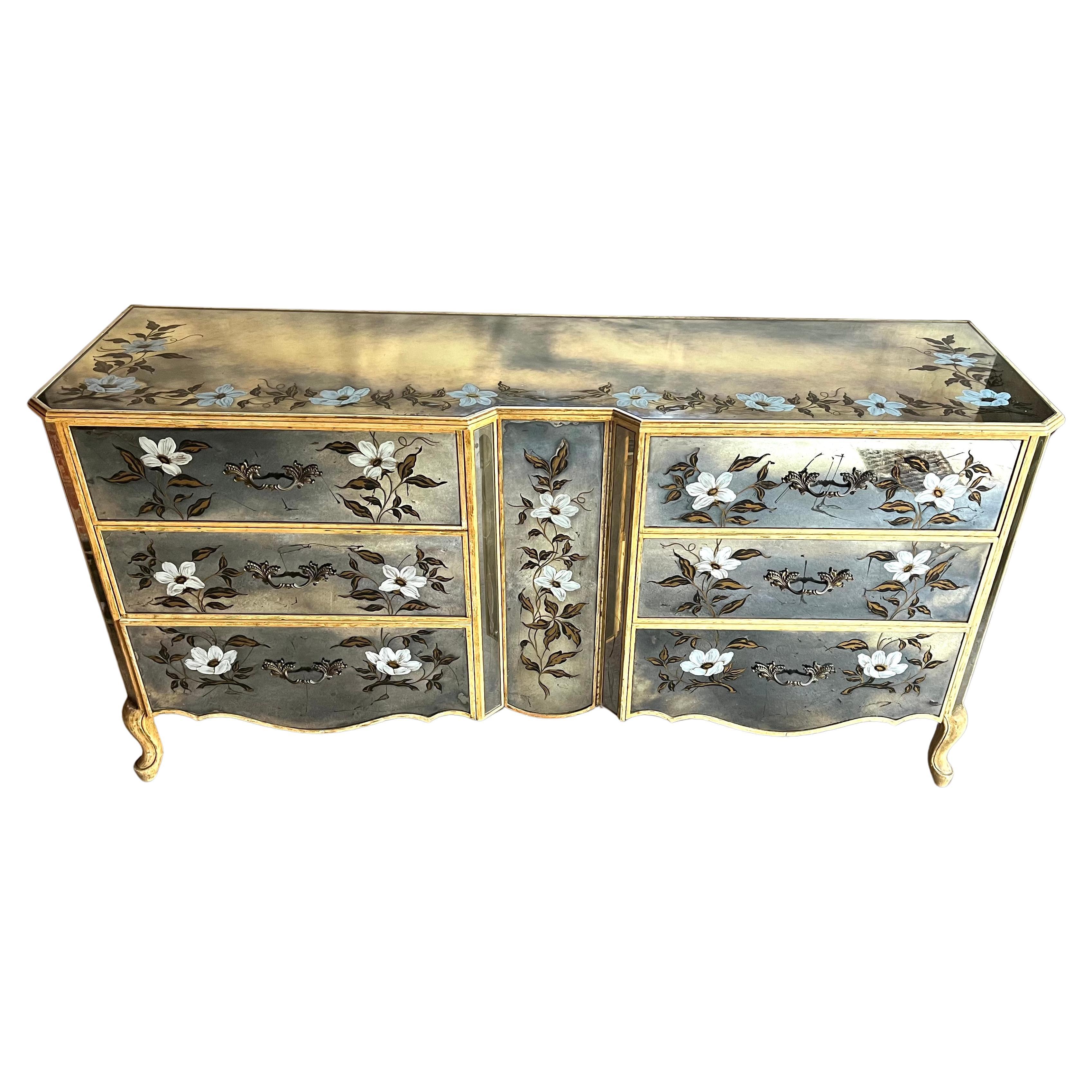 A whimsical verre eglomise double commode in the Hollywood Regency/Louis XV Style, circa 1950, decorated with reverse painted inset mirrors featuring white Clematis flowers and vines, the piece consists of 6 large drawers with a hinged door