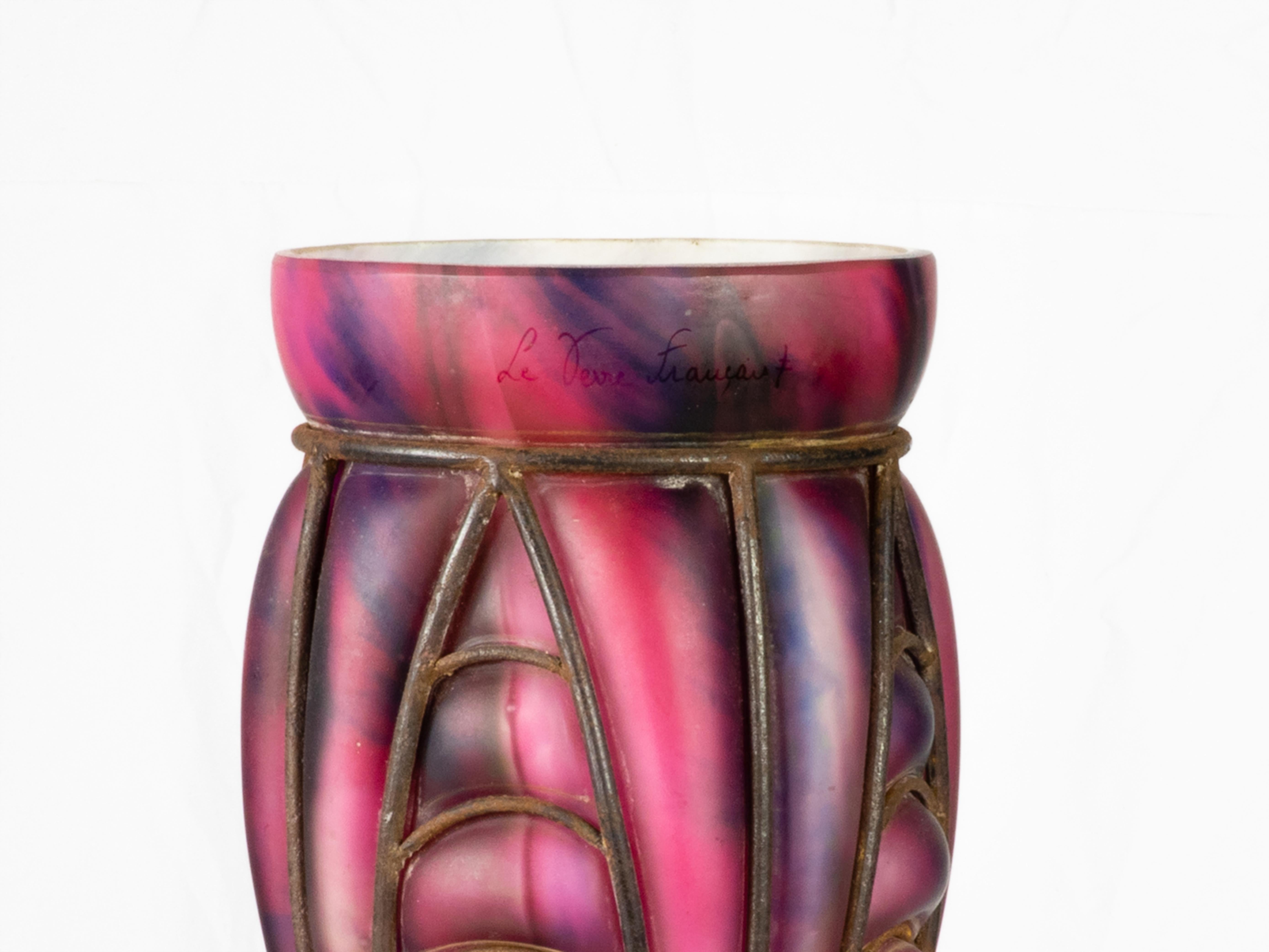 Eine Glasvase der Verrerie D'Art Lorrain mit schmiedeeisernem Panzer im Majorelle-Stil aus Croismare in der Nähe von Nancy, einem der Zentren  der Glasherstellung.
Es zeigt einen rosa und violett marmorierten Oberkörper mit einem graugrünen