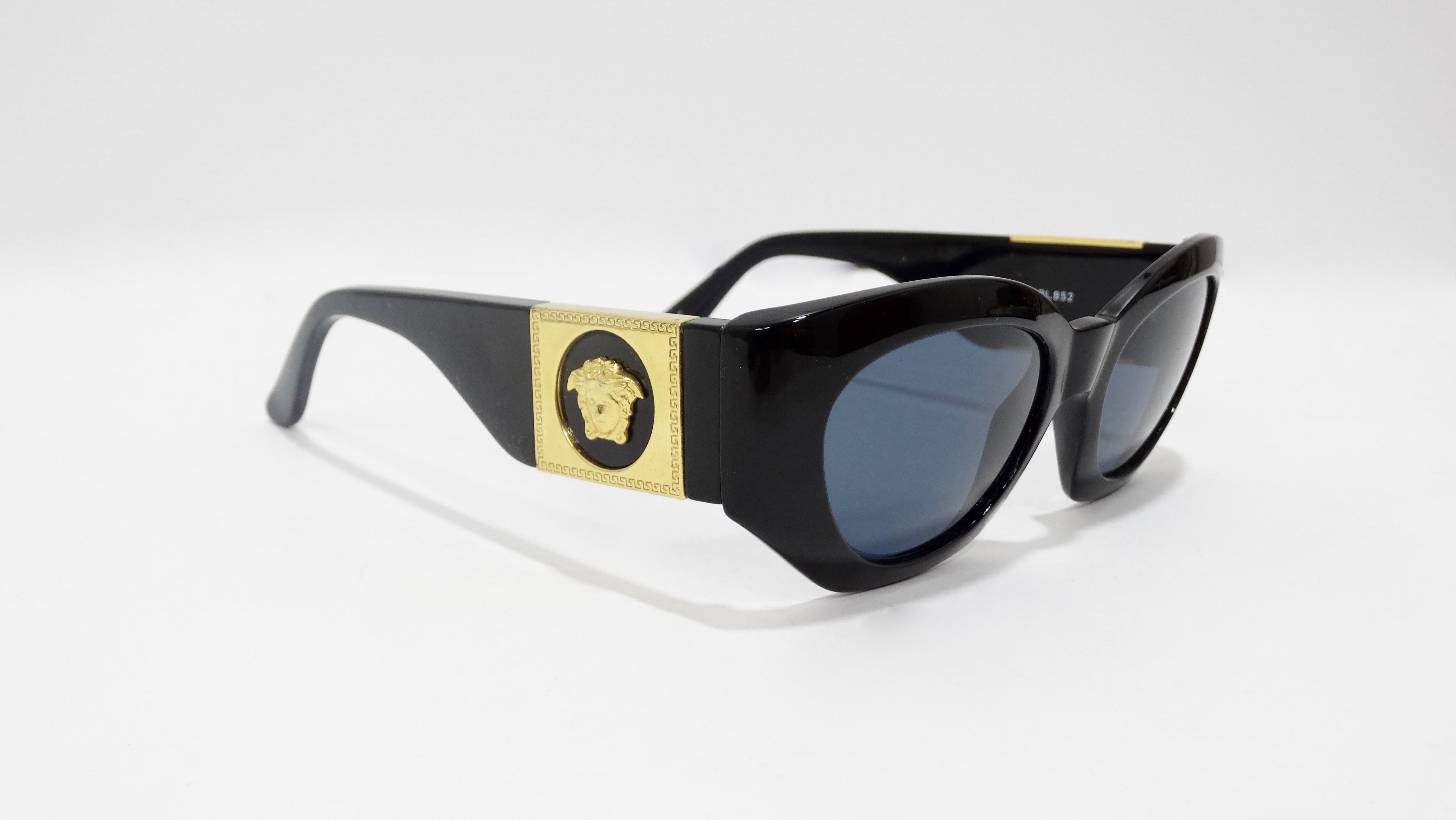 Your new everyday sunnies are here! Circa late 1980s, these Versace sunglasses feature a black frame, dark blue lenses, and a subtle cat eye shape. On both arms are gold toned Medusa heads with the signature Greek key. Signed Gianni Versace Made in