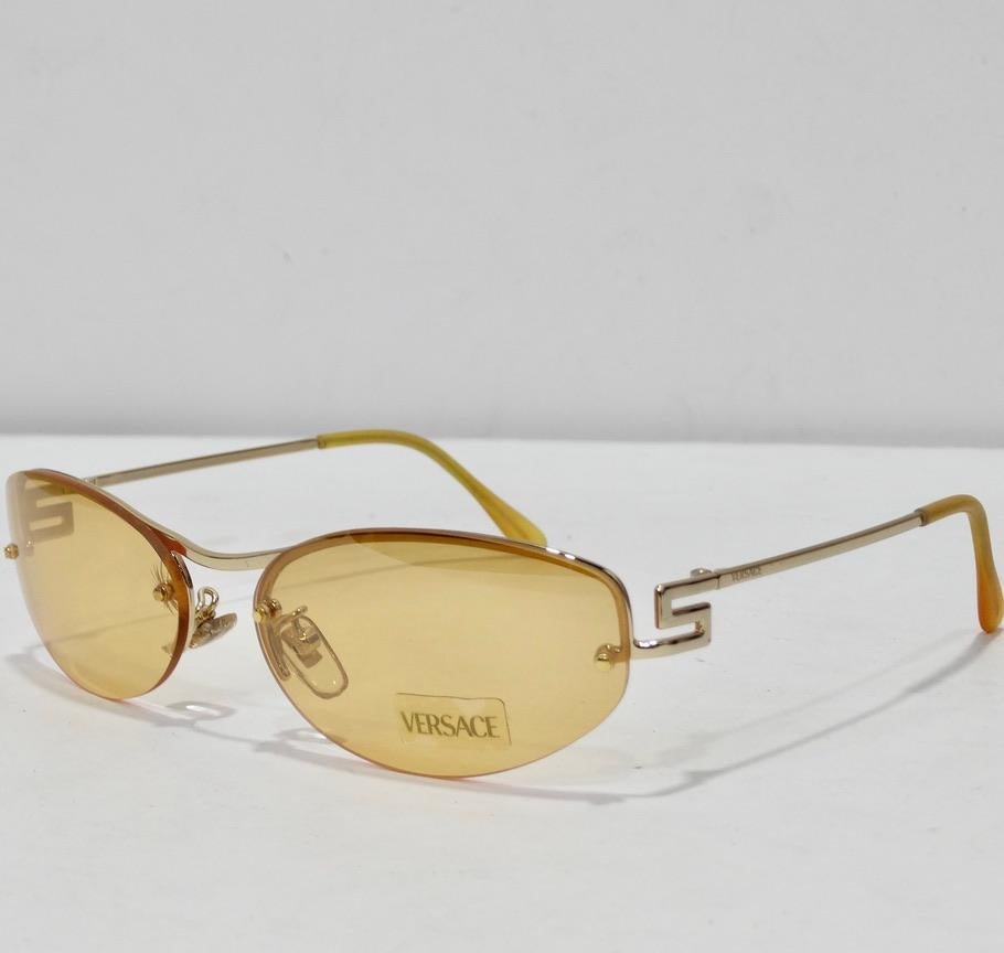 Wie umwerfend ist diese Versace-Sonnenbrille aus dem Lagerbestand der 1990er Jahre?! Perfekt für alle, die einen ovalen Rahmen lieben. Die Brille hat gelbe Gläser und hellorangefarbene Details mit goldfarbenen Akzenten. Die perfekte Sonnenbrille für
