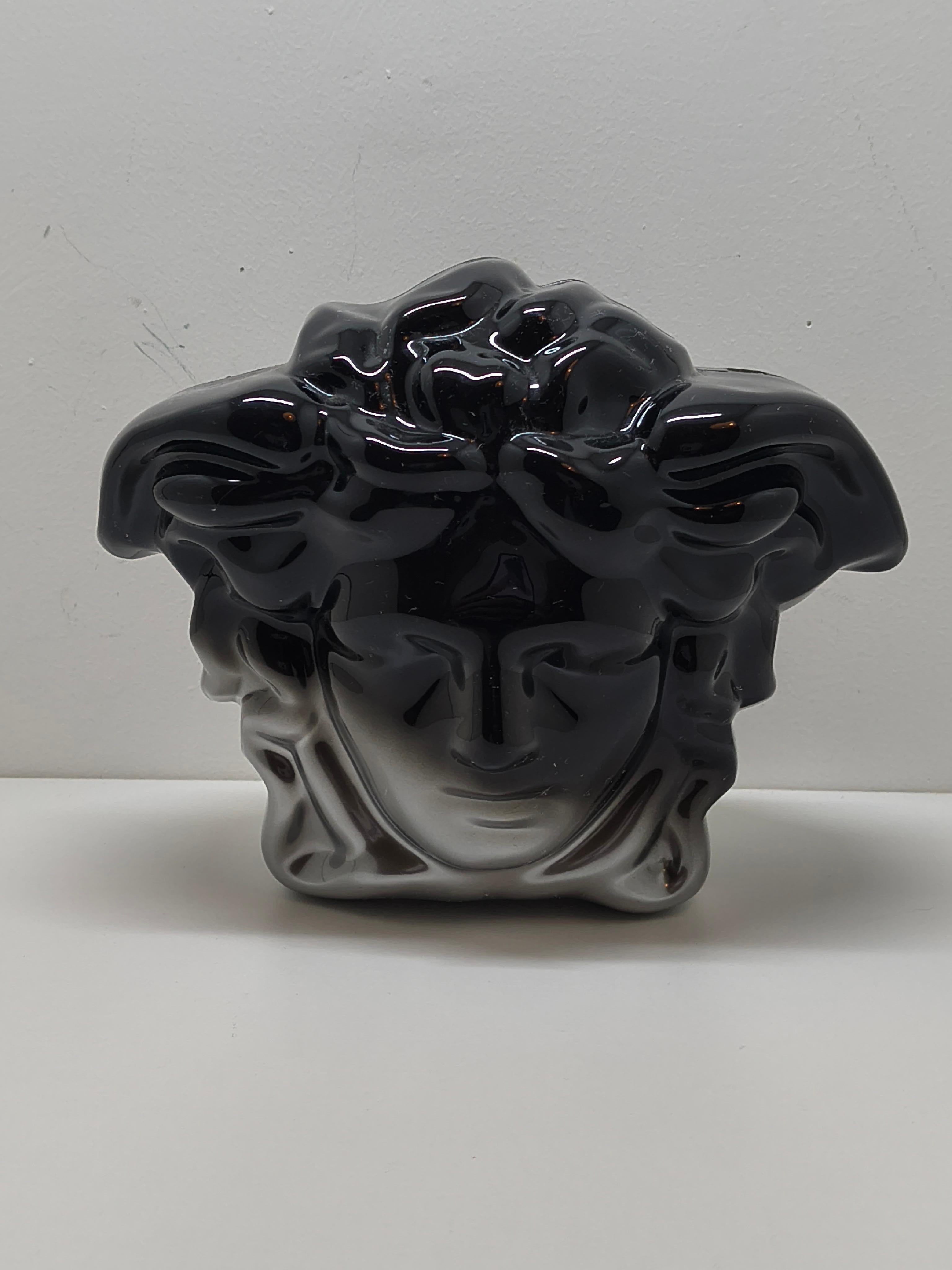 Llama la atención con este atrevido y escultural bolso Versace, diseñado con la inconfundible forma de la icónica cabeza de Medusa. Fabricada en acrílico negro brillante, esta pieza estructurada es a la vez una obra de arte y una declaración de