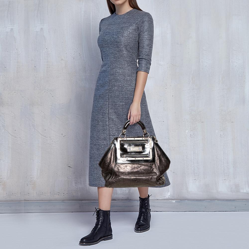 Diese Handtasche aus dem Hause Versace ist ein wahr gewordener Traum für jede Fashionista. Verleihen Sie sich einen luxuriösen Look mit dieser Schultertasche aus Leder und Lackleder und zeigen Sie Ihren Stil. Die Tasche ist innen mit Satin