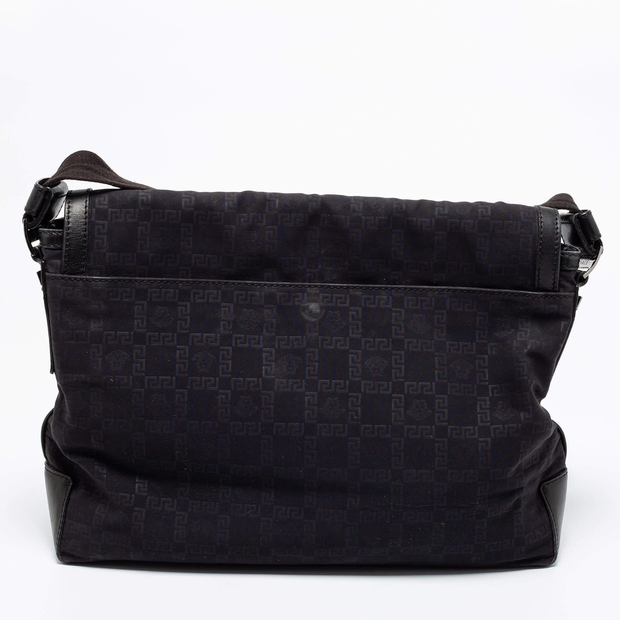 Diese schwarze Tasche von Versace ist ein praktisches Accessoire, das sich auf Reisen oder bei täglichen Besorgungen als äußerst nützlich erweisen wird. Sie ist aus charakteristischem Nylon gefertigt und verfügt über einen Lederboden, einen langen