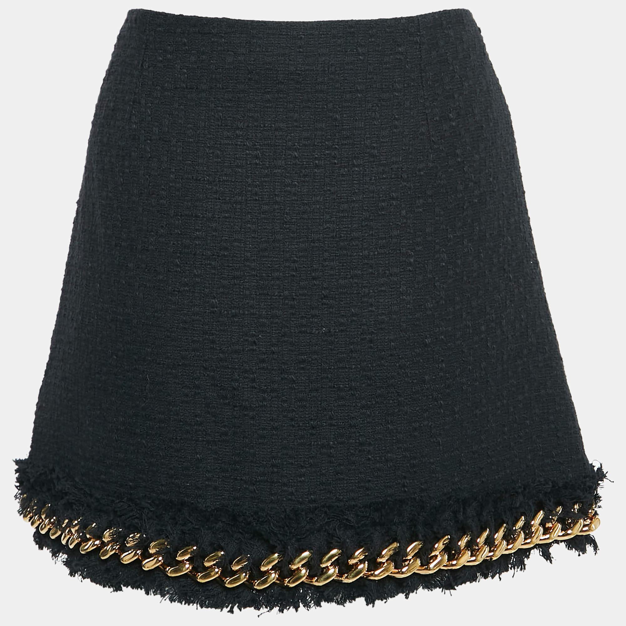 La falda Versace presenta un diseño elegante y sofisticado confeccionado en tweed negro de alta calidad. Esta minifalda se acentúa con atrevidas inserciones de cadenas que añaden un toque vanguardista a su silueta clásica. Perfecto para llamar la