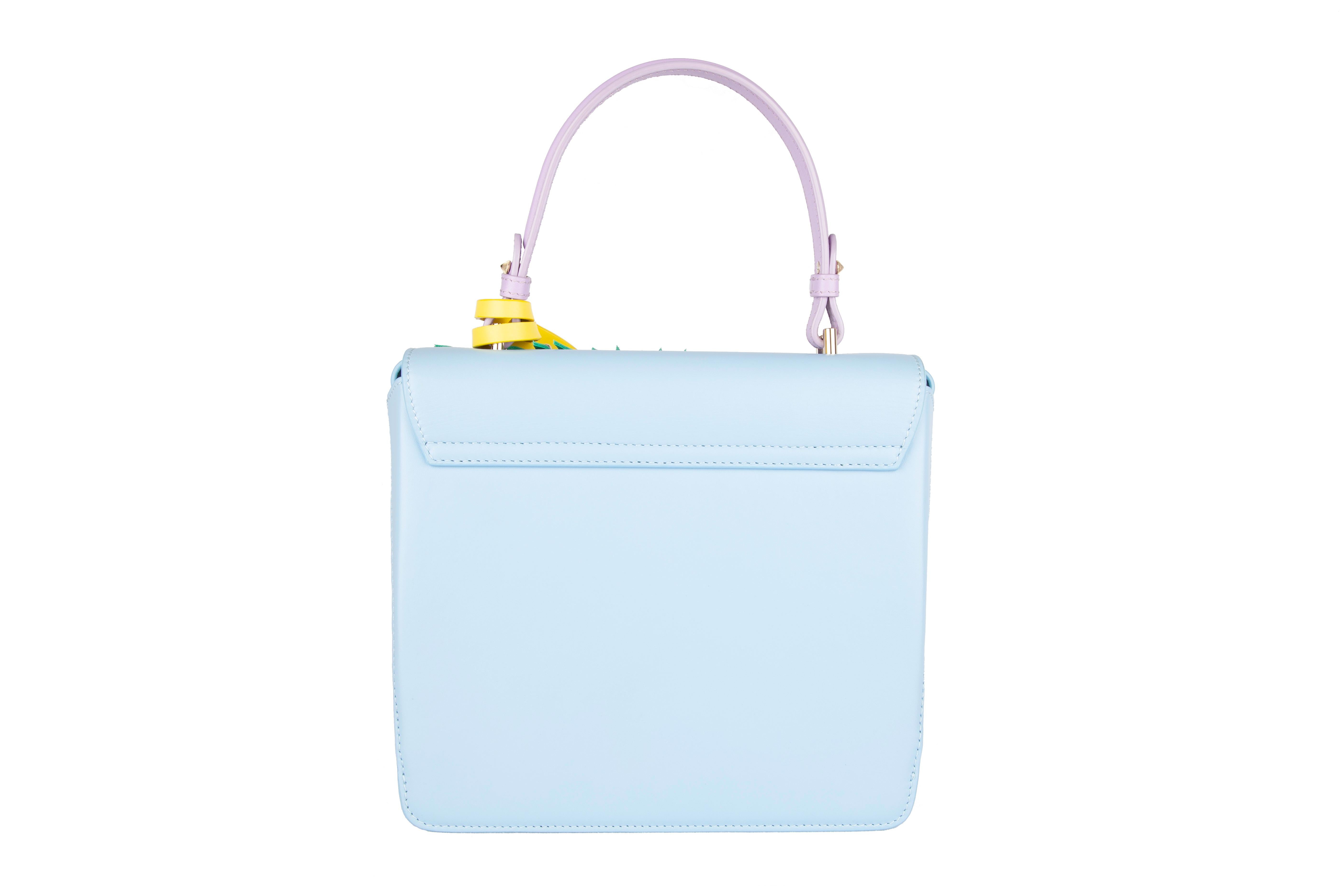 Crafted in Italy from lambskin leather, this Versace DV One top handle bag features a palm frond leather design, silver tone studs and hardware, leather strap, a lavender top handle, and a yellow tag. The DV One bags are no longer in production,