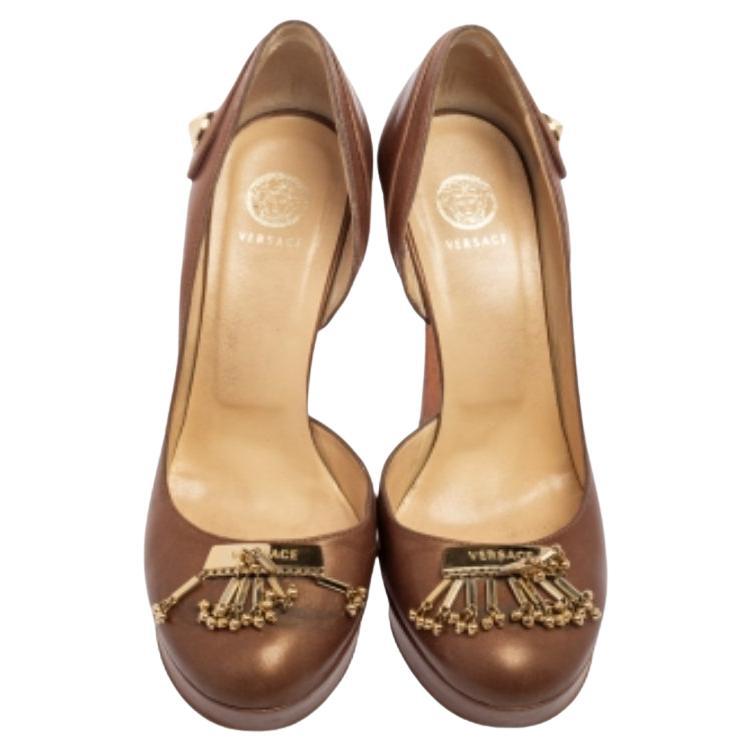 With an elegant d'Orsay cut, this pair of Versace pumps will be a valuable addition to your wardrobe. Covered in brown leather, it is decorated with gold-tone accents and the brand plaque on the round toe. The 13cm heels are supported by platforms
