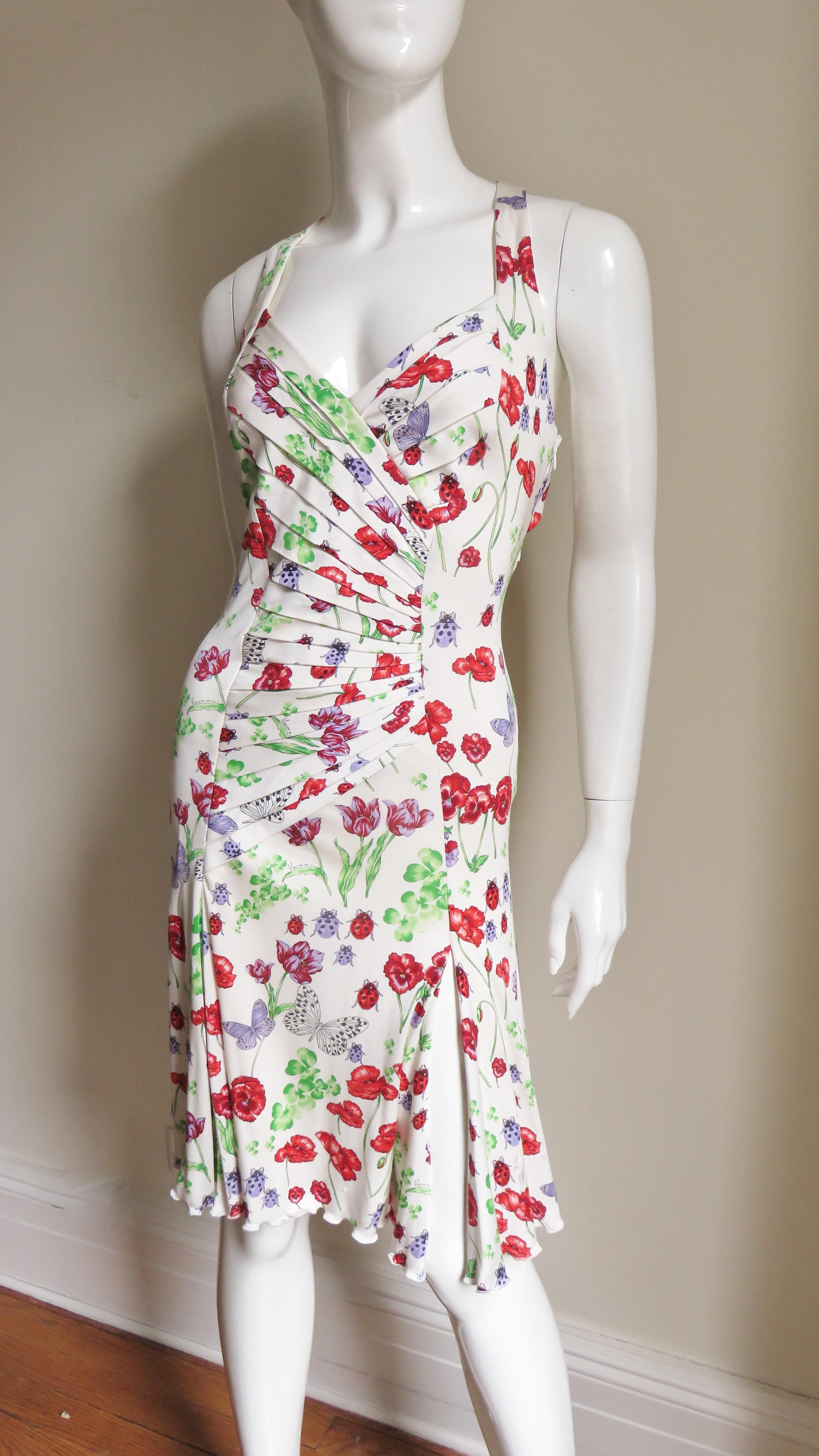 A beautiful fine white silk jersey dress from Versace with a flowers and butterflies pattern in red, purple and green. It has a plunging neckline, a crossing front tucked bodice and shoulder straps crossing the upper portion of a largely nude back.