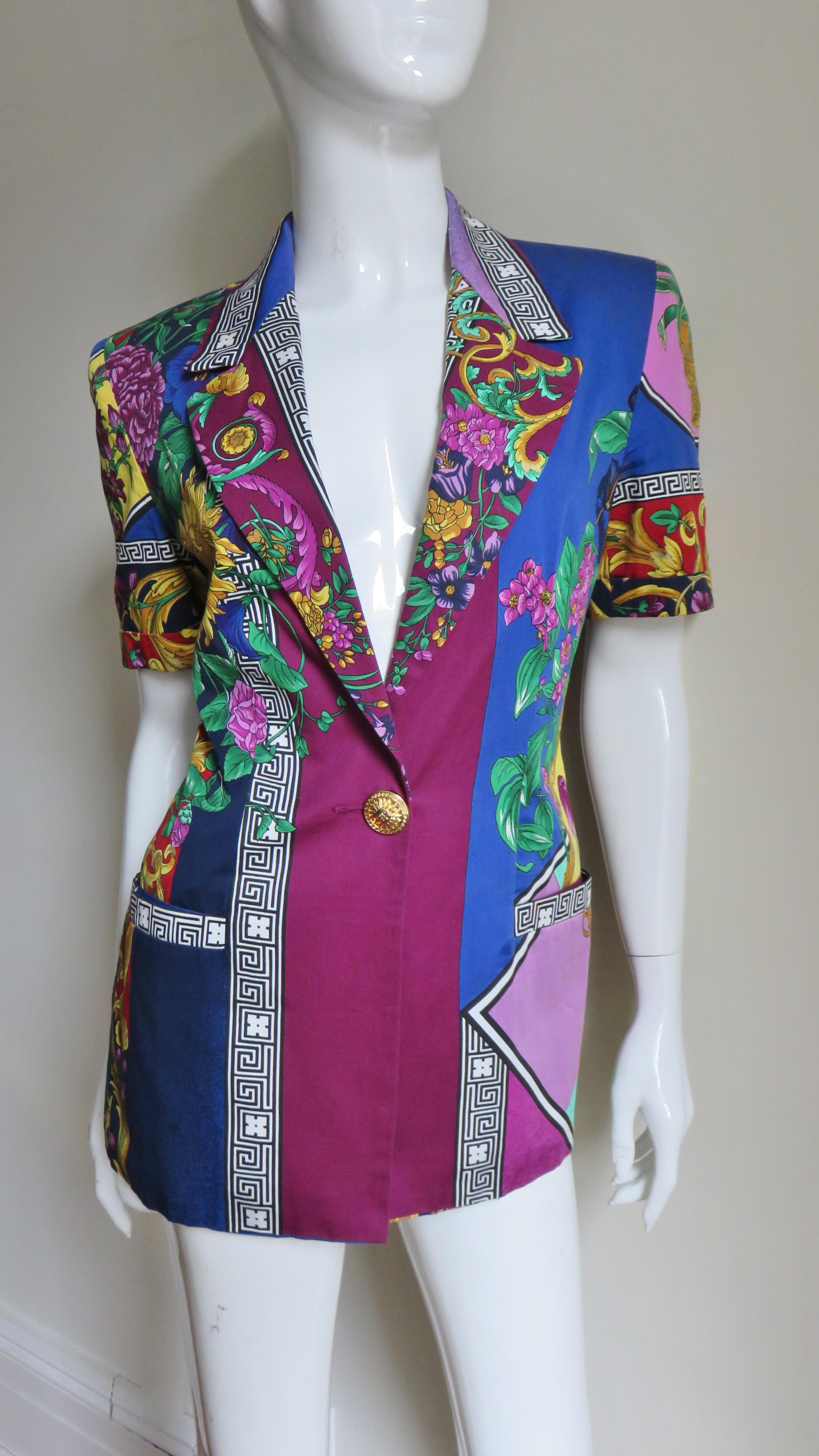 A fabulous short sleeve jacket from Versace Jeans Couture with an elaborate pattern of flowers, leaves, scrolls and Greek Keys Versace is known for in bright colors.  It has a lapel collar, short cuffed sleeves, small shoulder pads and closes with