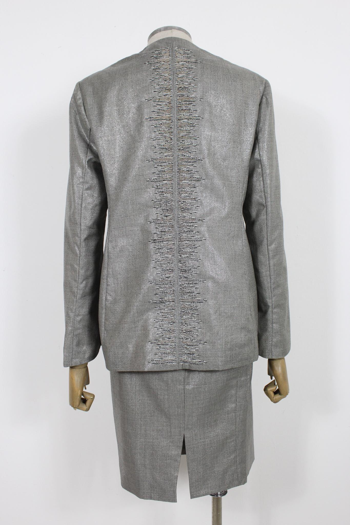 This vintage Versace Couture 90s skirt suit is a true statement piece. The gray lamè wool fabric gives off a luxurious shine and is lined with silk for added comfort. The elegant suit features intricate embroidery behind the shoulder, adding a touch