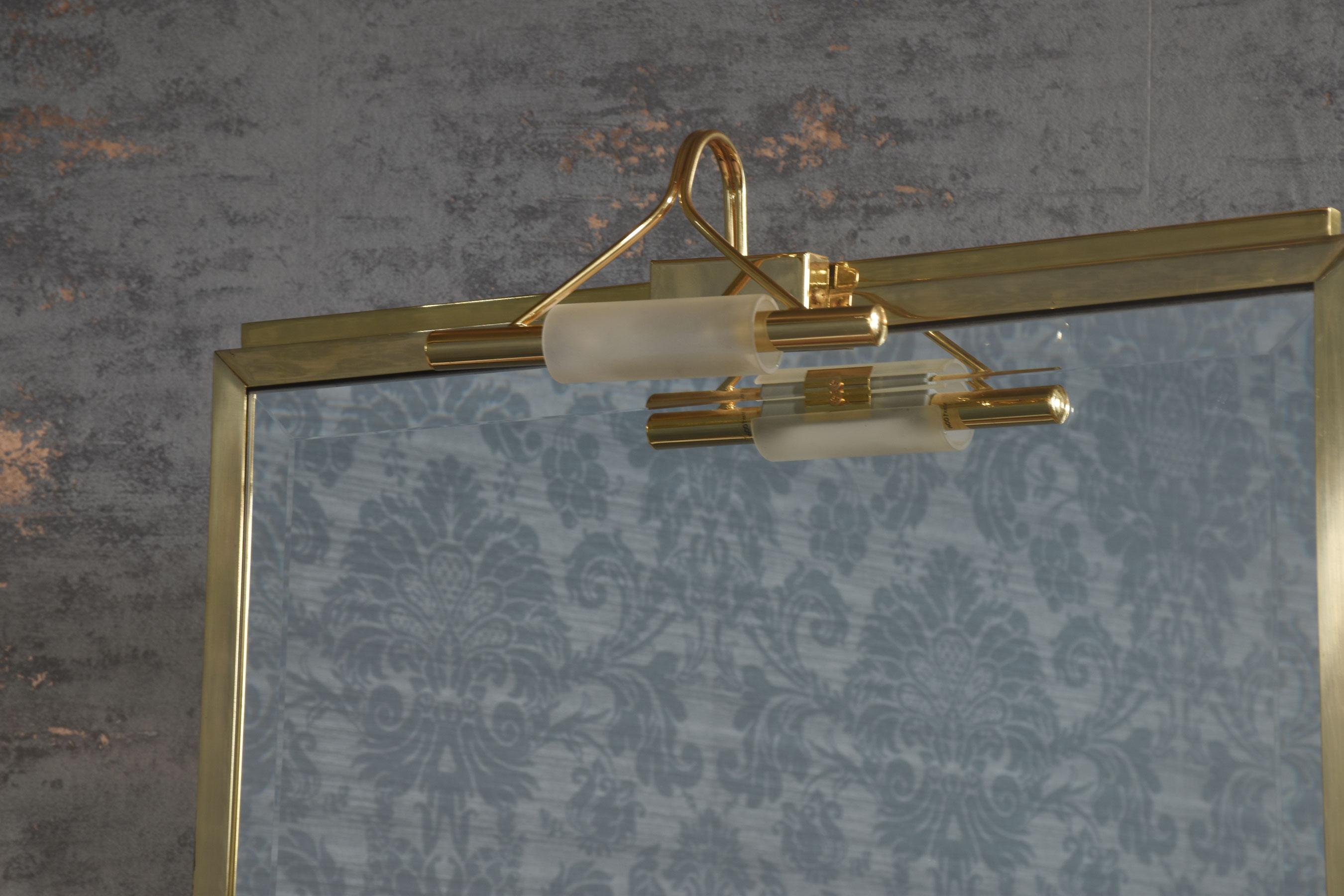Specchio da toilette bifacciale Versace, la grande lastra di specchio smussata su entrambi i lati è circondata da una cornice in ottone, un lato della quale è dotato di una lampada funzionante. La base è sostenuta da pilastri in mogano ben