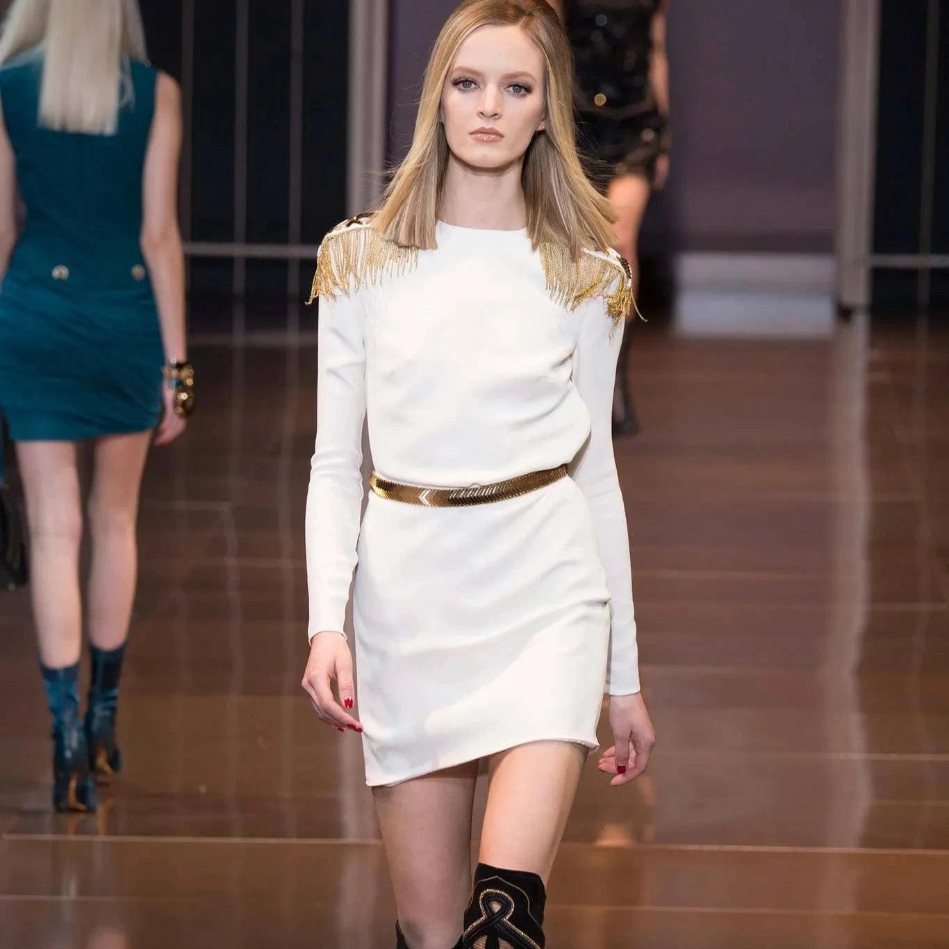 Versace white silk dress from Fall 2014 with golden belt and detachable chain-draped shoulder embellishments. Military style, bold and structured design.
 Also seen on Heidi Klum at an America’s Got Talent event. 
 Remarks: there are some small