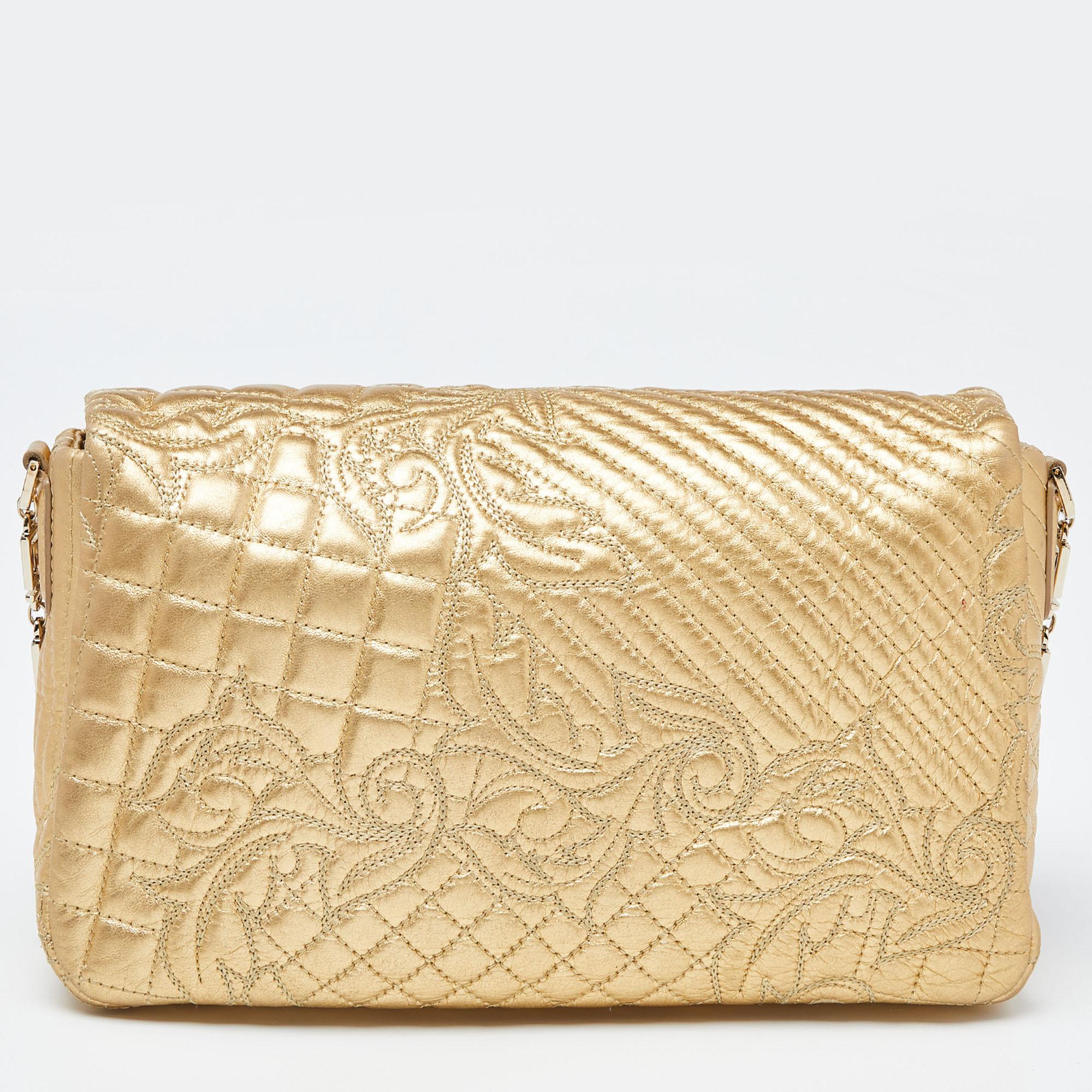 Comme ce sac de Versace est magnifique ! Confectionné en cuir doré et avec des accessoires en métal doré, il présente un design exceptionnel. Il possède un intérieur en satin sécurisé par des fermetures à glissière et il est retenu par une chaîne.