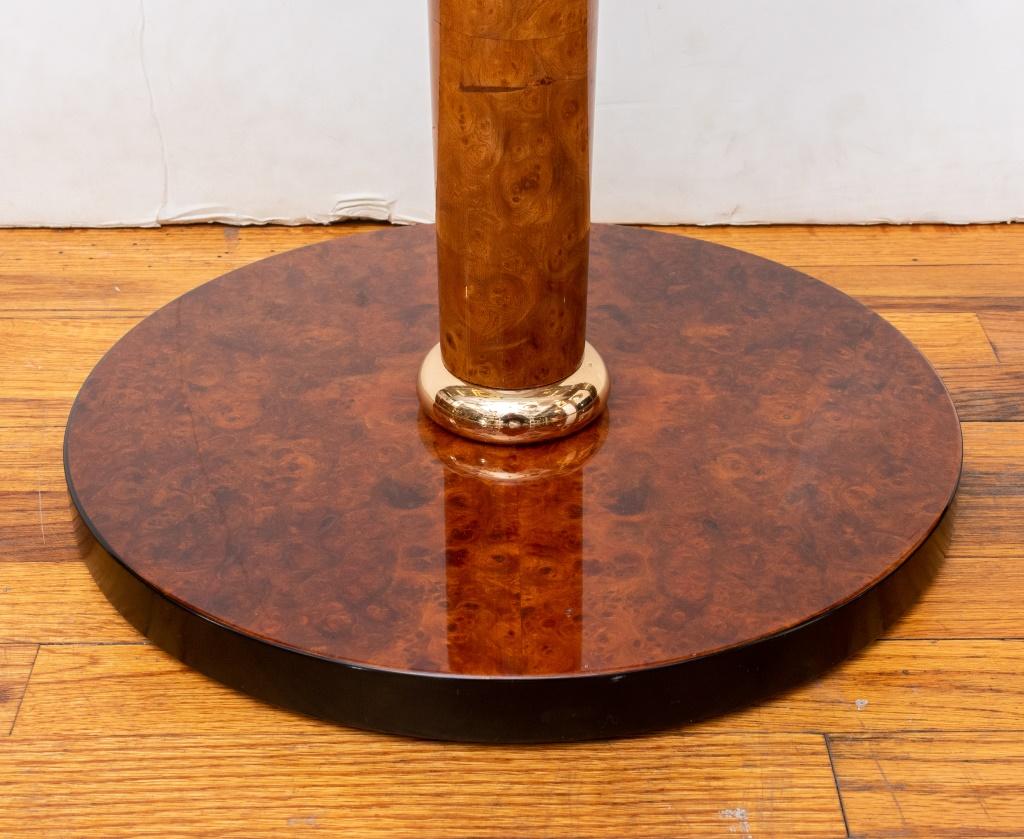 Tavolino Versace Home, con piano circolare in vetro sopra un supporto colonnare affusolato con finitura laccata in radica a fantasia su socle dorate sopra una base circolare, anch'essa con finitura simile. 24,5