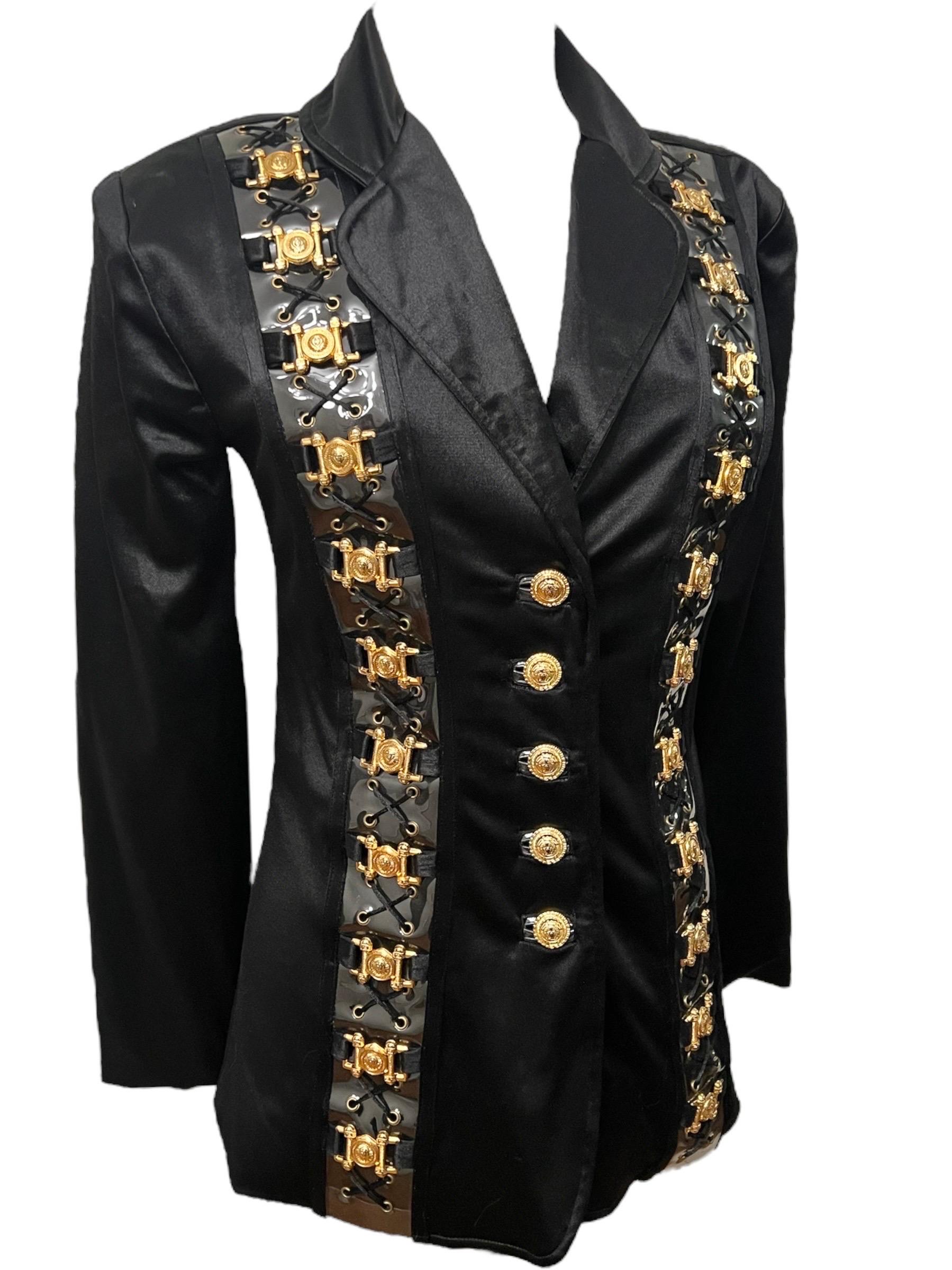 Fatti notare con questa straordinaria giacca vintage Versace Jeans Couture nera in stile bondage. Realizzata in un ricco tessuto di raso nero, questa giacca strutturata presenta gli iconici bottoni a medusa dorati sul davanti, spalle possenti,