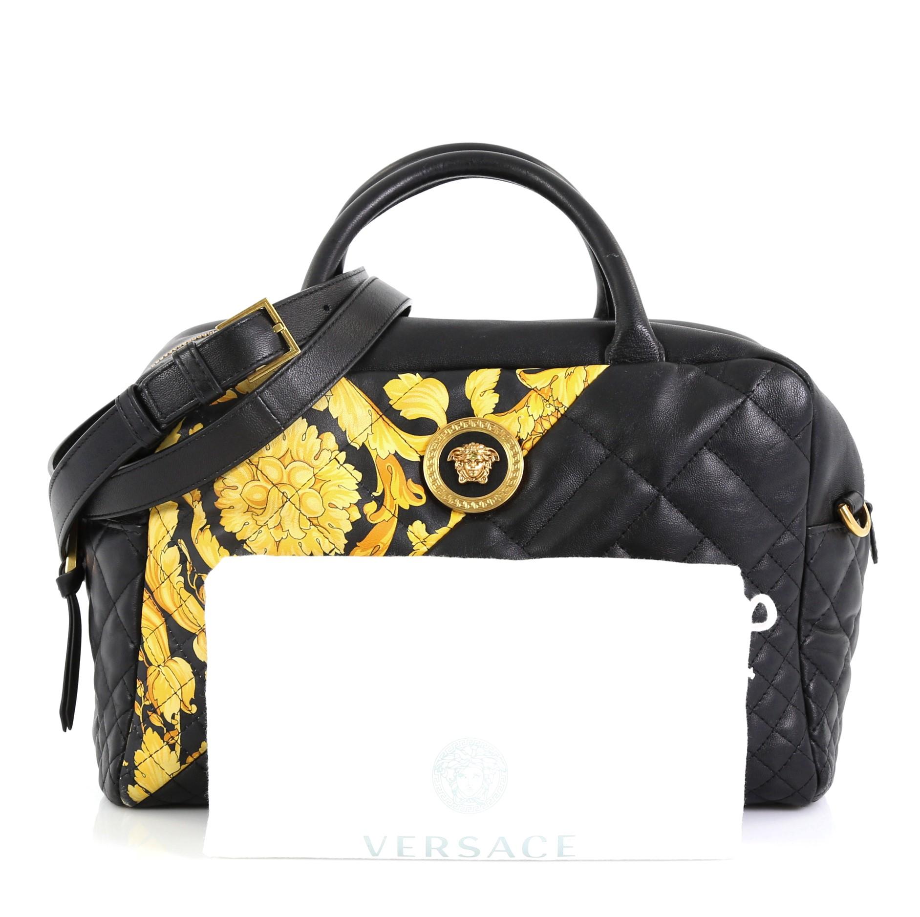 This Versace Medusa Convertible Satchel Quilted Printed Leather Medium, crafted from black quilted printed leather, features dual rolled handles, Medusa head at front, and gold-tone hardware. Its zip closure opens to a black fabric