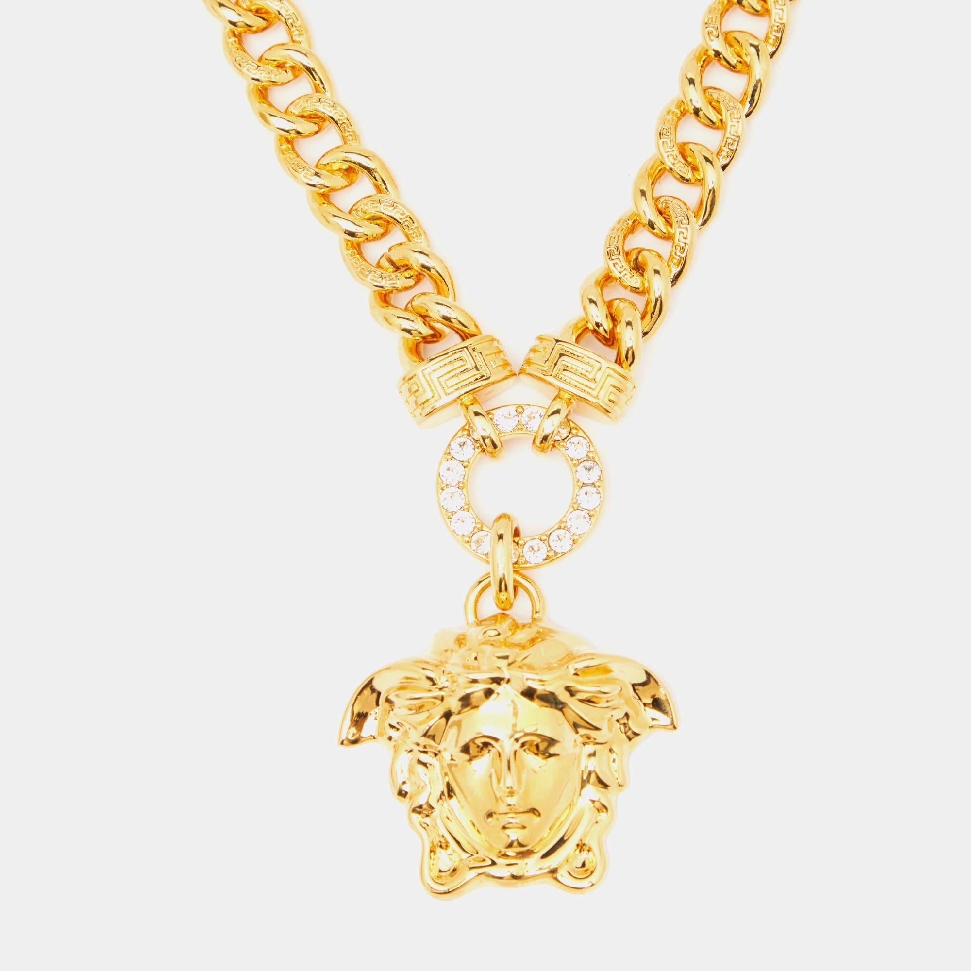Paré de l'allure opulente du collier Versace. Réalisée avec une attention méticuleuse aux détails, cette pièce exquise présente un emblème Medusa incrusté de cristaux étincelants, sur un fond doré lustré. Une déclaration intemporelle de luxe et de
