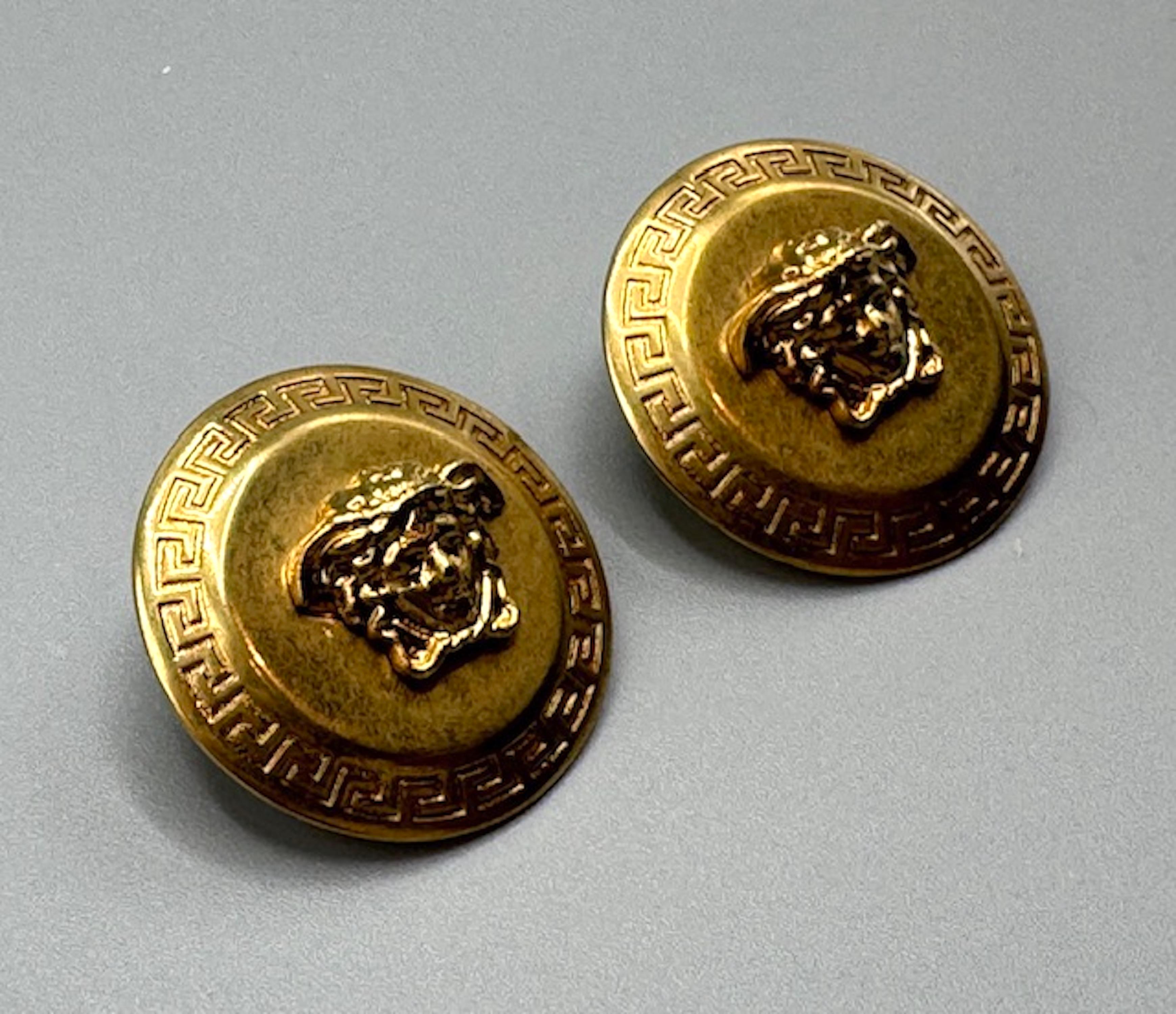 A a classic Greek style pair of button earrings with the iconic Vesace Medusa head. The head of Medusa, a figure from Greek mythology. Gianni Versace, the founder of the Italian luxury fashion company, chose Medusa as the logo because he believed