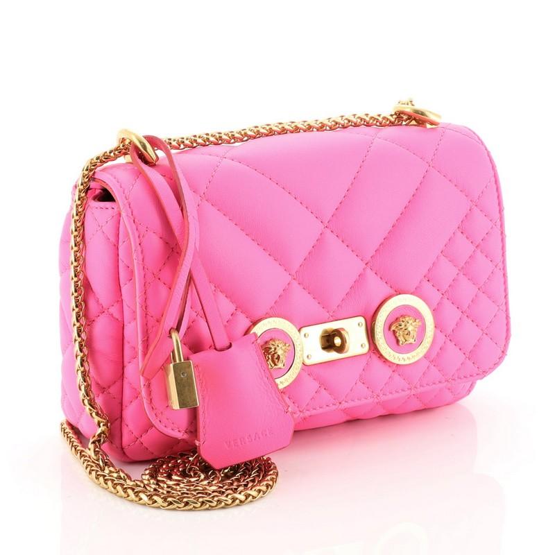 This Versace Medusa Padlock Icon Flap Bag Quilted Leather Small, crafted in pink leather, features a sliding Greek chain shoulder strap, flap top with Medusa head medallions and gold-tone hardware. Its turn-lock closure opens to a black fabric