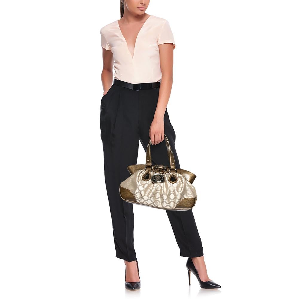 La borsa Madonna di Versace è realizzata in tela e pelle metallizzata. È dotata di due manici, finiture dorate e un ciondolo con logo sul davanti. È foderata in raso all'interno e potrà contenere facilmente le tue necessità.

