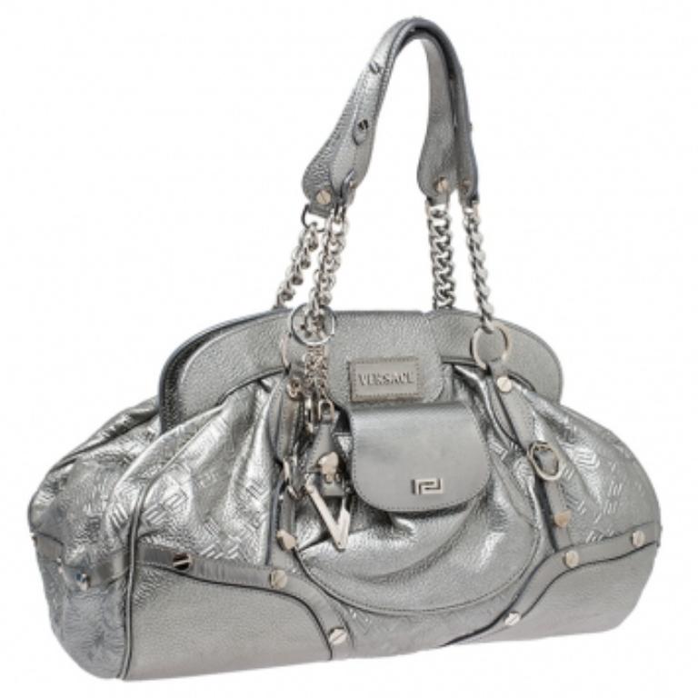 Designed in a unique and wonderful silhouette, this satchel from Versace will be a special addition to any closet. It is crafted from metallic silver leather and is accented with studs on the exterior along with a flap pocket at the front. The bag