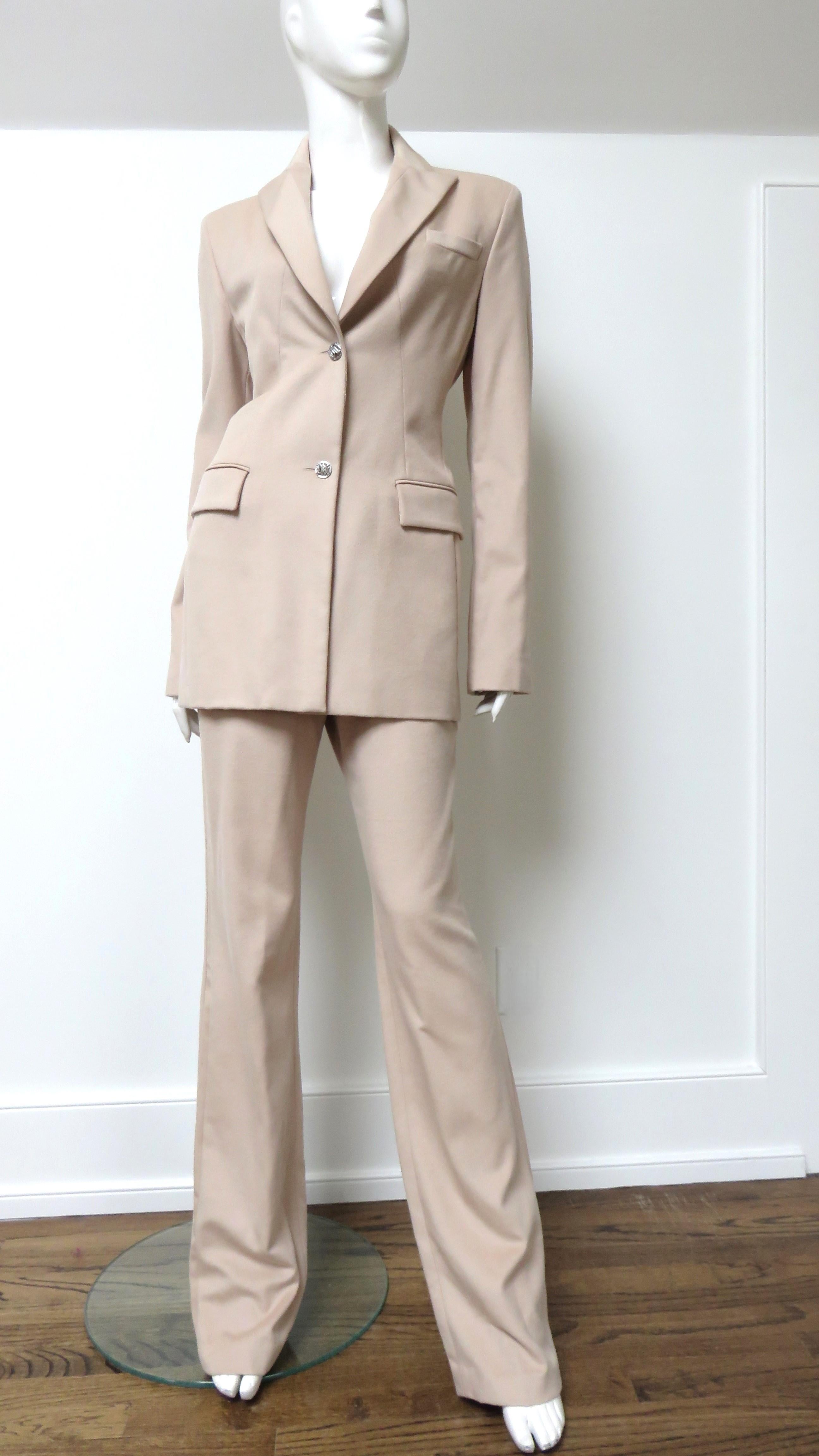 Ein wunderschöner, leichter Hosenanzug aus beiger Wolle von Versace. Die Jacke ist länger geschnitten, hat einen Reverskragen, Paspeltaschen vorne, einen Rückenschlitz und aufwändig eingesetzte, geformte, feine Paneele aus demselben Stoff in einer