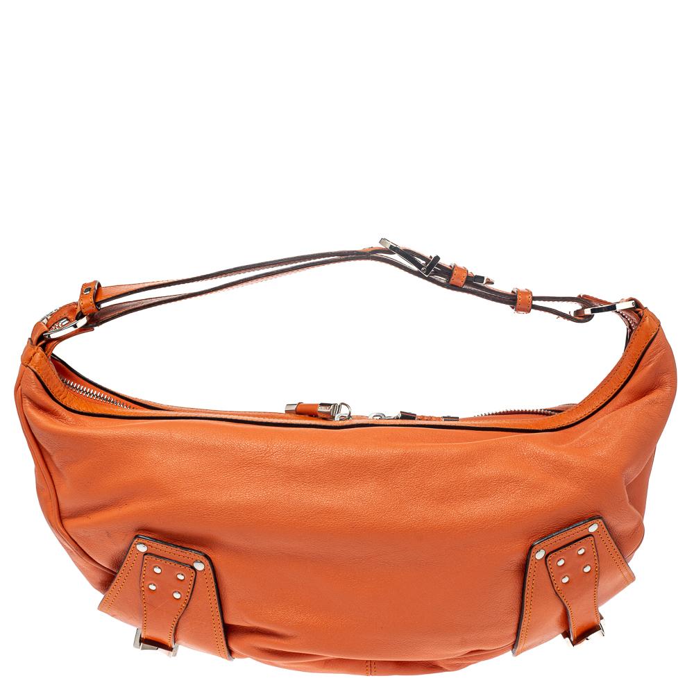 Made by Versace, this handbag is an immaculate balance of sophistication and rational utility. Designed with quality leather, this bag comes in a lovely shade of orange. This bag has a spacious interior lined with satin. The two pockets in the front