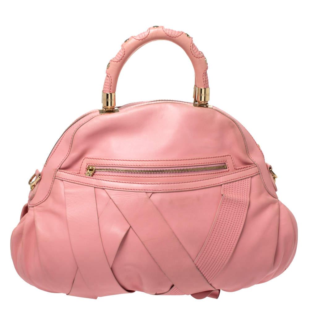 Auf diese hübsche Schleifen-Tasche von Versace können Sie sich verlassen, wenn es um einen besonderen Look geht. Die Tasche ist aus rosafarbenem Leder gefertigt und mit goldfarbenen Beschlägen verziert. Diese elegante Schönheit verfügt über zwei