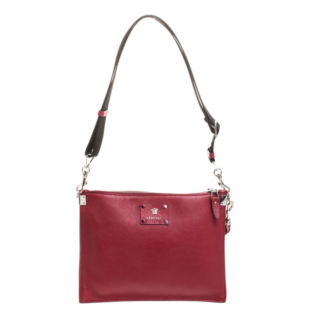 This striking shoulder bag hails from the iconic house of Versace. Crafted in Italy, it is made of quality leather and flaunts a lovely shade of red. It is held by a single handle and features a lovely silhouette. The front has been beautified with