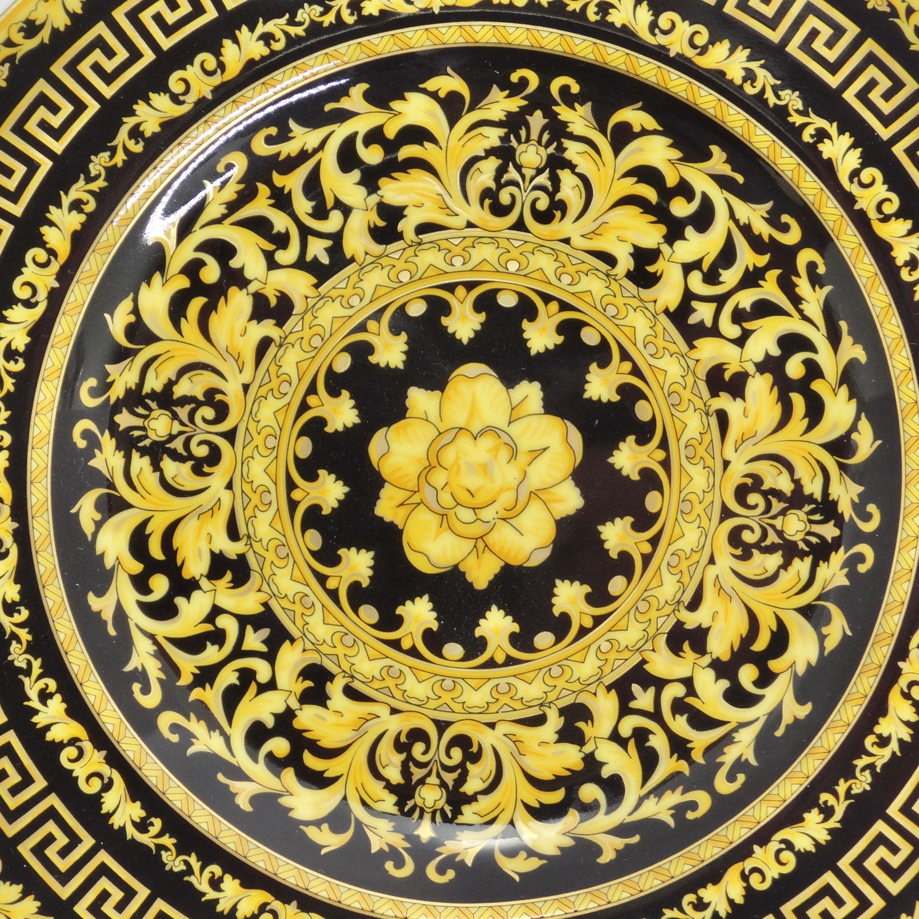 Introducing the Versace Rosenthal 1990s Porcelain Floral Gold Plate, a classic dinner plate that encapsulates the timeless elegance of Versace's signature style. This exquisite piece features a striking black and gold baroque print, showcasing the