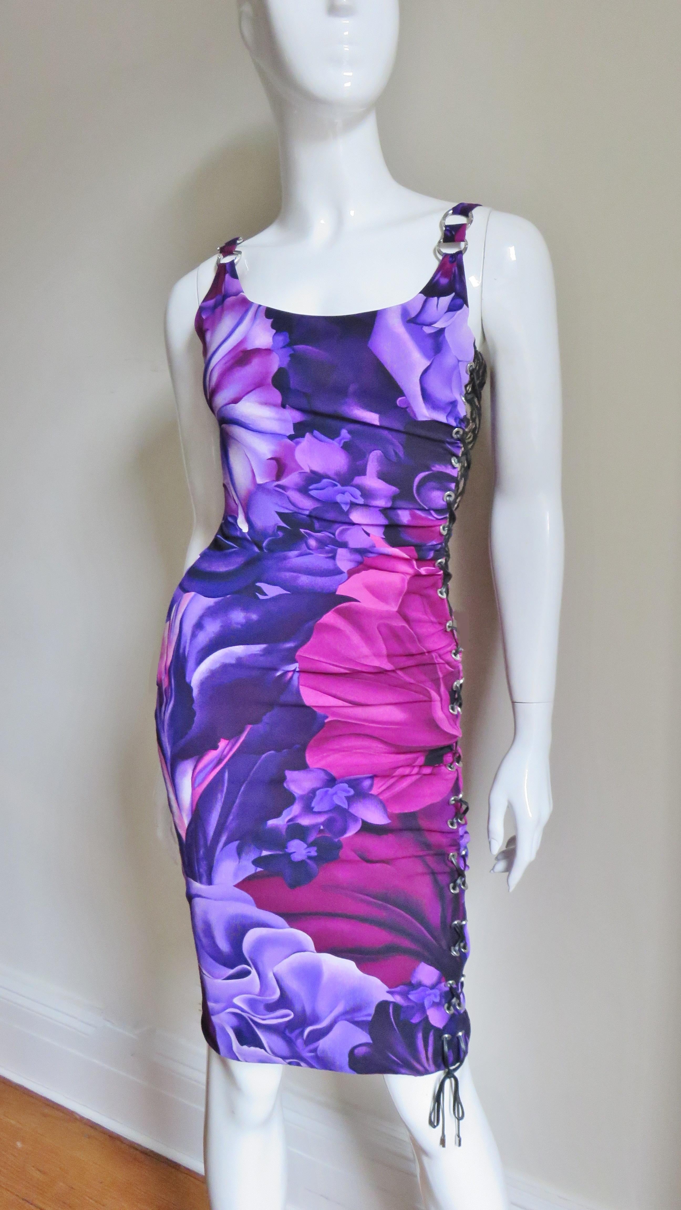 A great flower pattern stretch silk dress in pinks, purples and black from Versace. It has a scoop neckline with metal ring decorated shoulder straps. It is semi fitted with ruching across the dress front and back. The left side laces up with fine