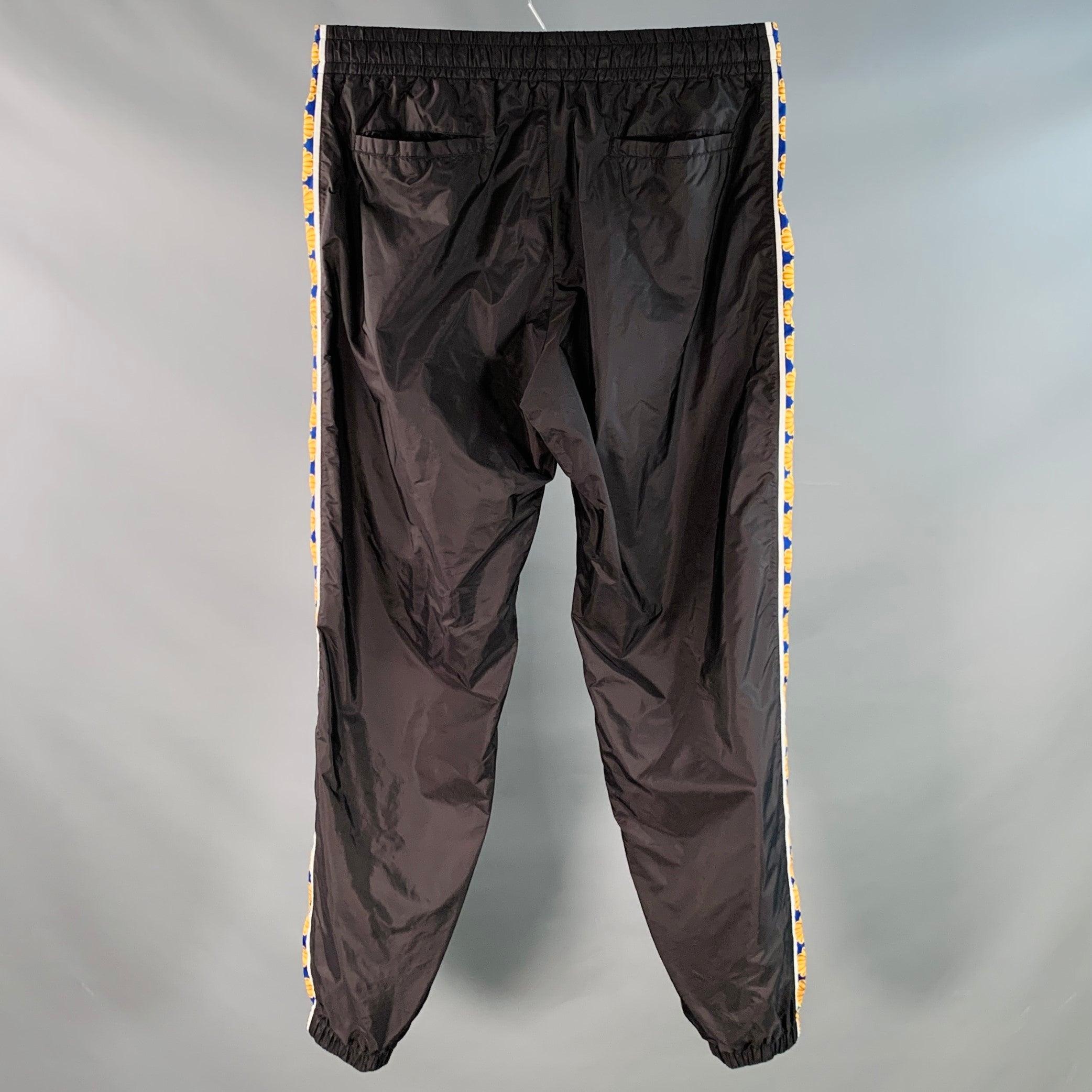 VERSACE sweatpants
in a black nylon featuring blue and gold tone side stripes, elastic cuffs, and drawstring waistband. Made in Italy.Excellent Pre-Owned Condition. 

Marked:   IT 52 

Measurements: 
  Waist: 34 - 38 inches Rise: 11 inches Inseam: