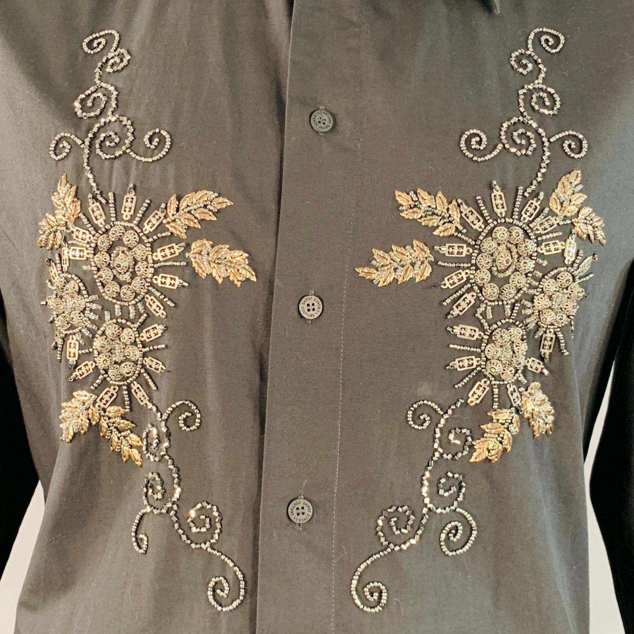 Langärmeliges Hemd von VERSACE JEANS COUTURE aus schwarzem Baumwollgewebe mit spitzem Kragen, goldfarbenem, floralem Perlenmuster und Knopfverschluss. Sehr guter gebrauchter Zustand. Kleines Zeichen. 

Markiert:   L 

Abmessungen: 
 
Schultern: 17,5